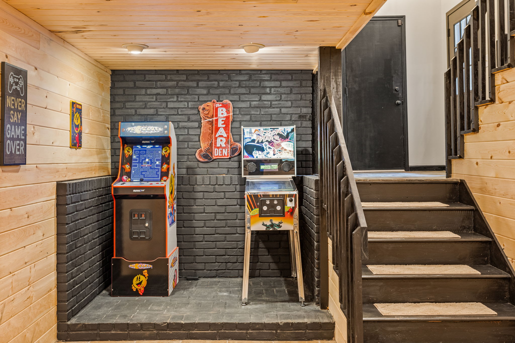 Retro Arcade Nook by the Stairs – A stylish game corner with a classic arcade machine, brick accent wall, and warm lighting, adding a fun touch to the cabin.