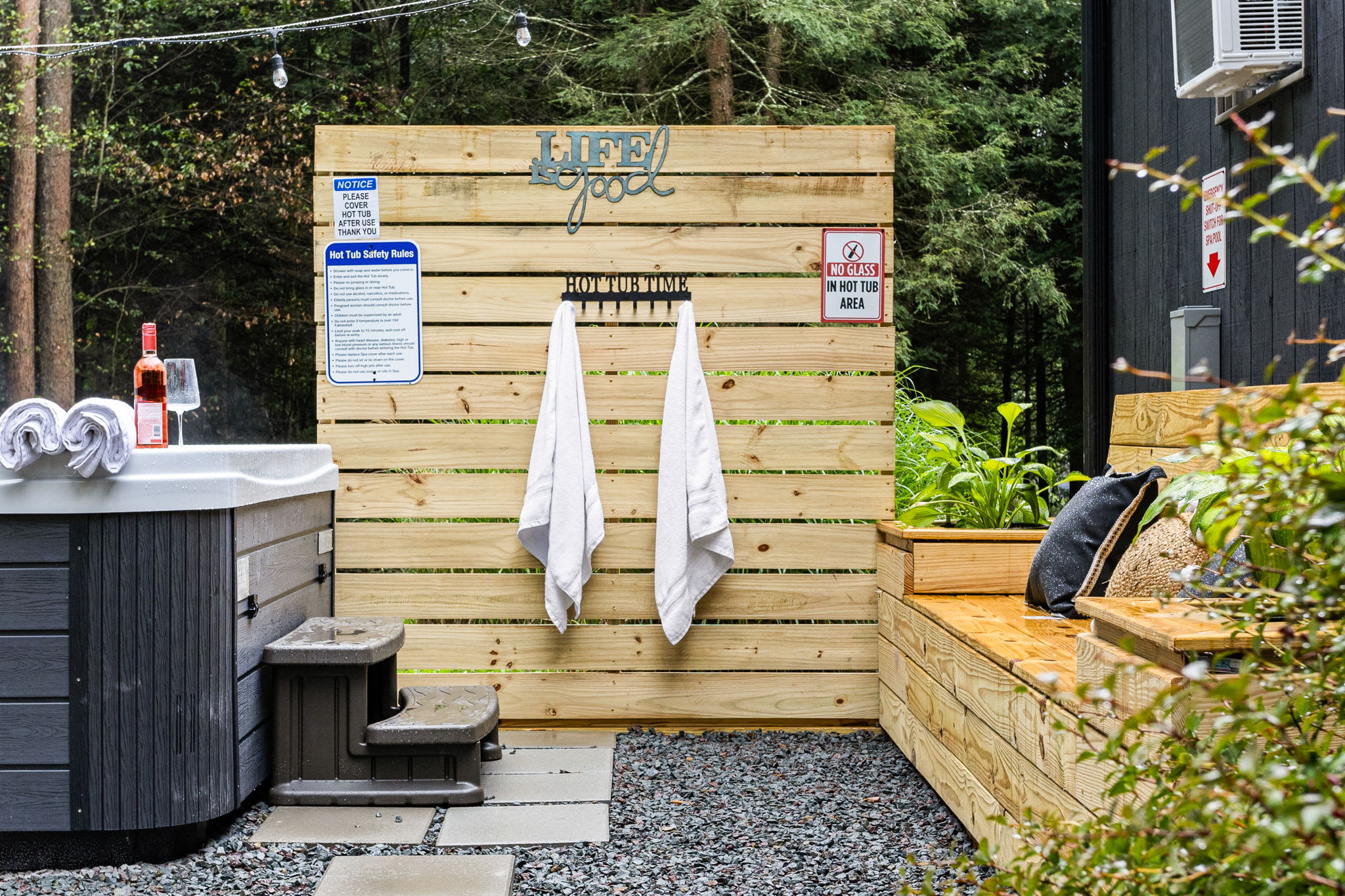 A private outdoor spa setup with a wooden privacy wall, towel hooks, and lush greenery for the ultimate relaxation experience.