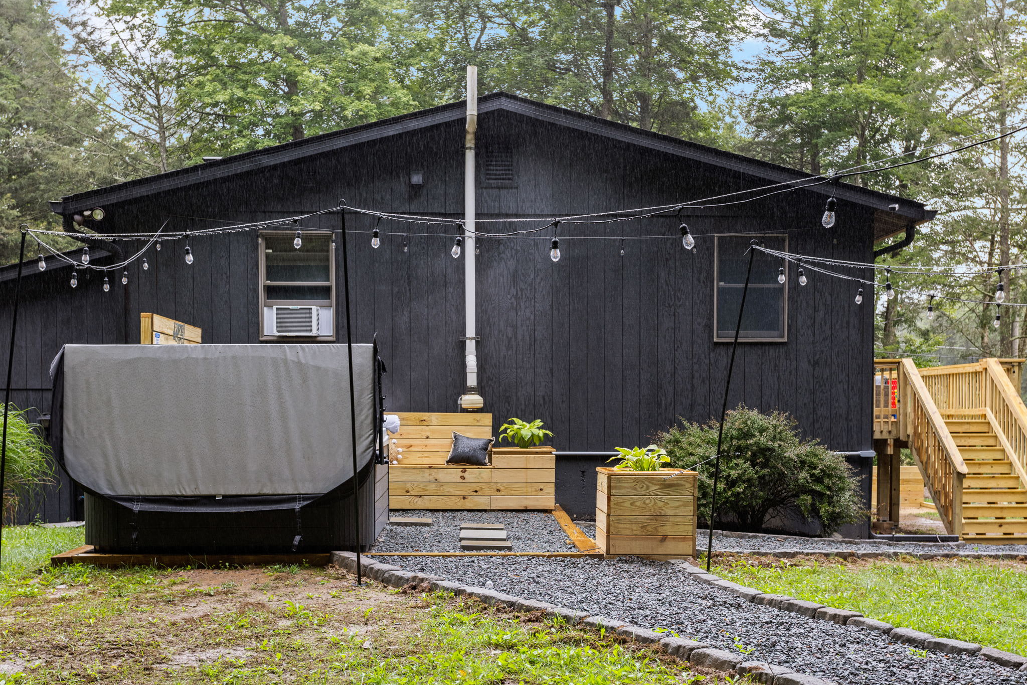 A beautifully designed outdoor space featuring a covered hot tub, wooden steps, and a stylish modern cabin exterior.