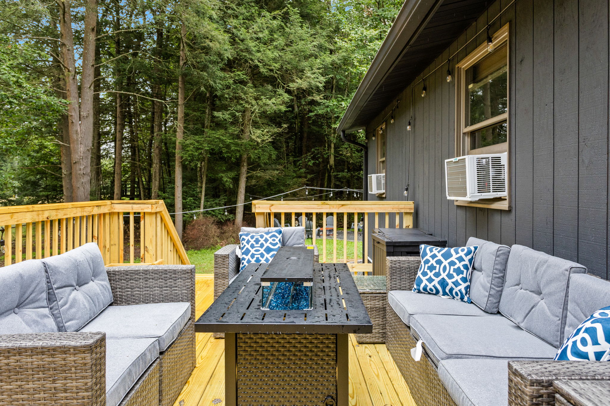 A stylish deck setup featuring plush sectional seating, decorative pillows, and a fire table, perfect for evening relaxation.