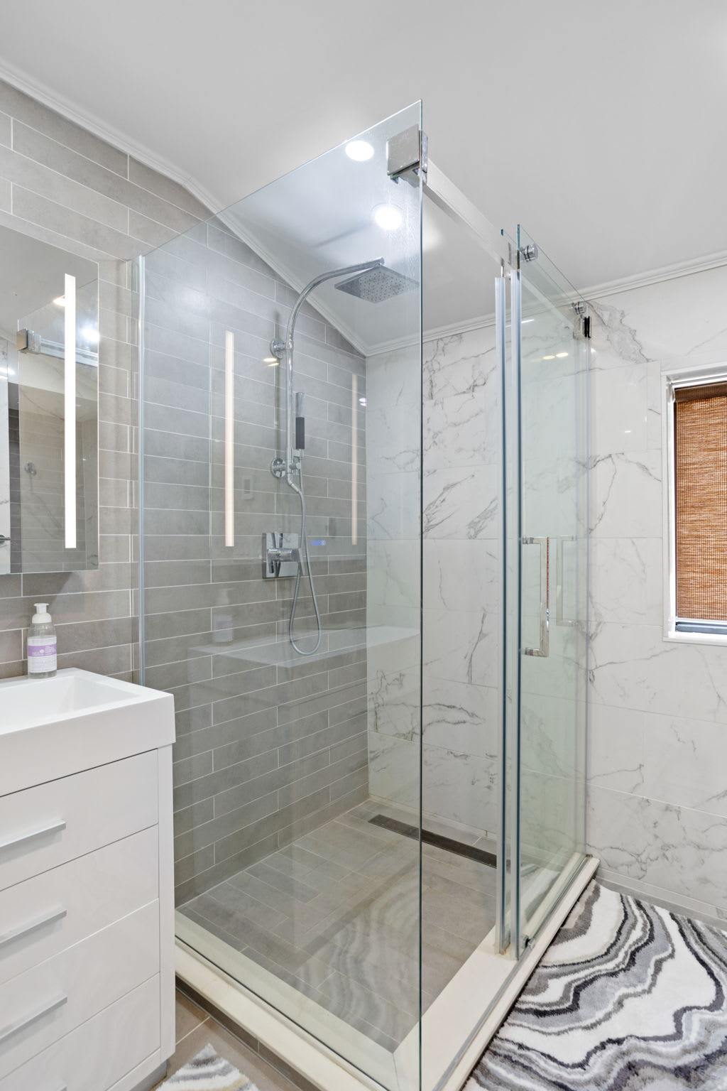 Experience ultimate relaxation in this luxurious glass-enclosed shower, complete with a rainfall showerhead, sleek gray tiles, and a bright, open feel.