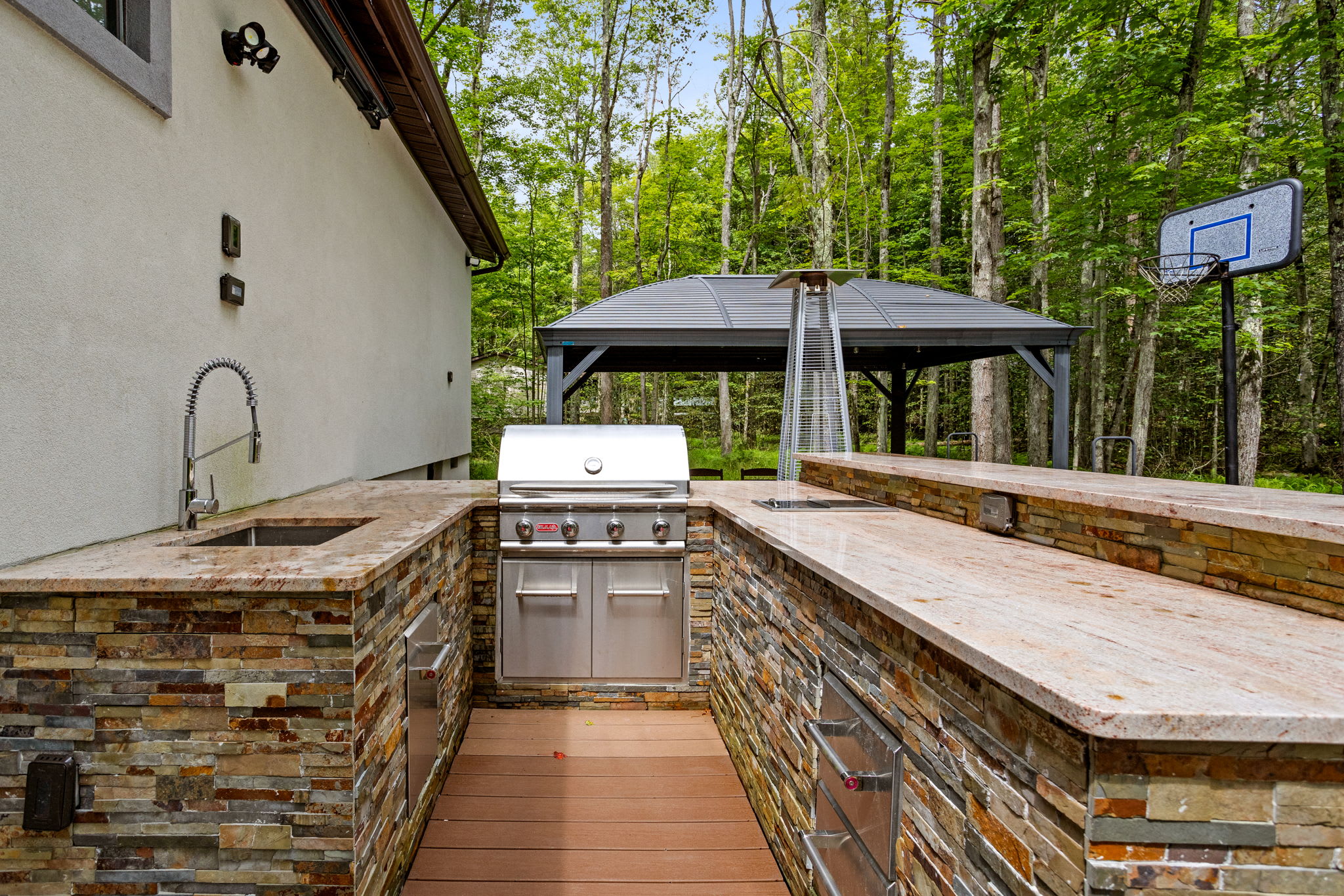 This built-in stone outdoor kitchen comes fully equipped with a high-end grill, sink, and ample counter space, perfect for summer cookouts and entertaining.
