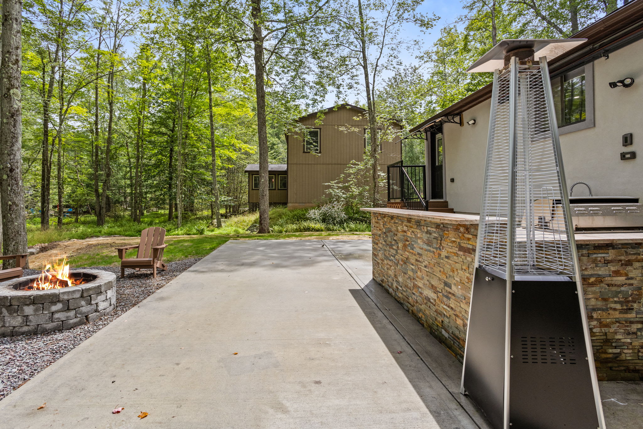 Whether you're staying warm by the firepit or the patio heater, this spacious outdoor area is designed for year-round enjoyment, surrounded by peaceful woodlands.