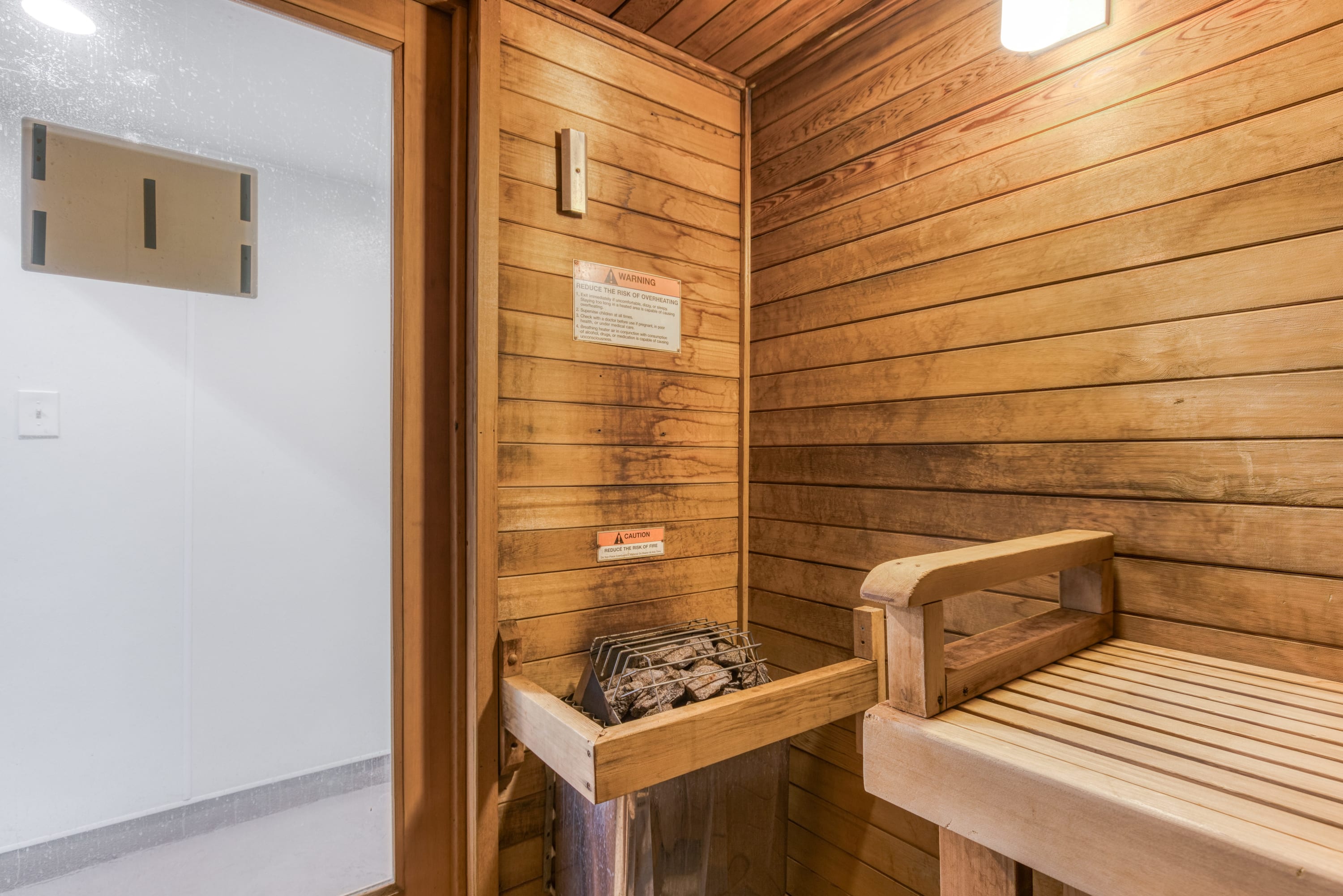 Close-up view inside a wooden sauna, highlighting the sauna heater with hot rocks and multi-level wooden benches, with a warning sign on the wall.