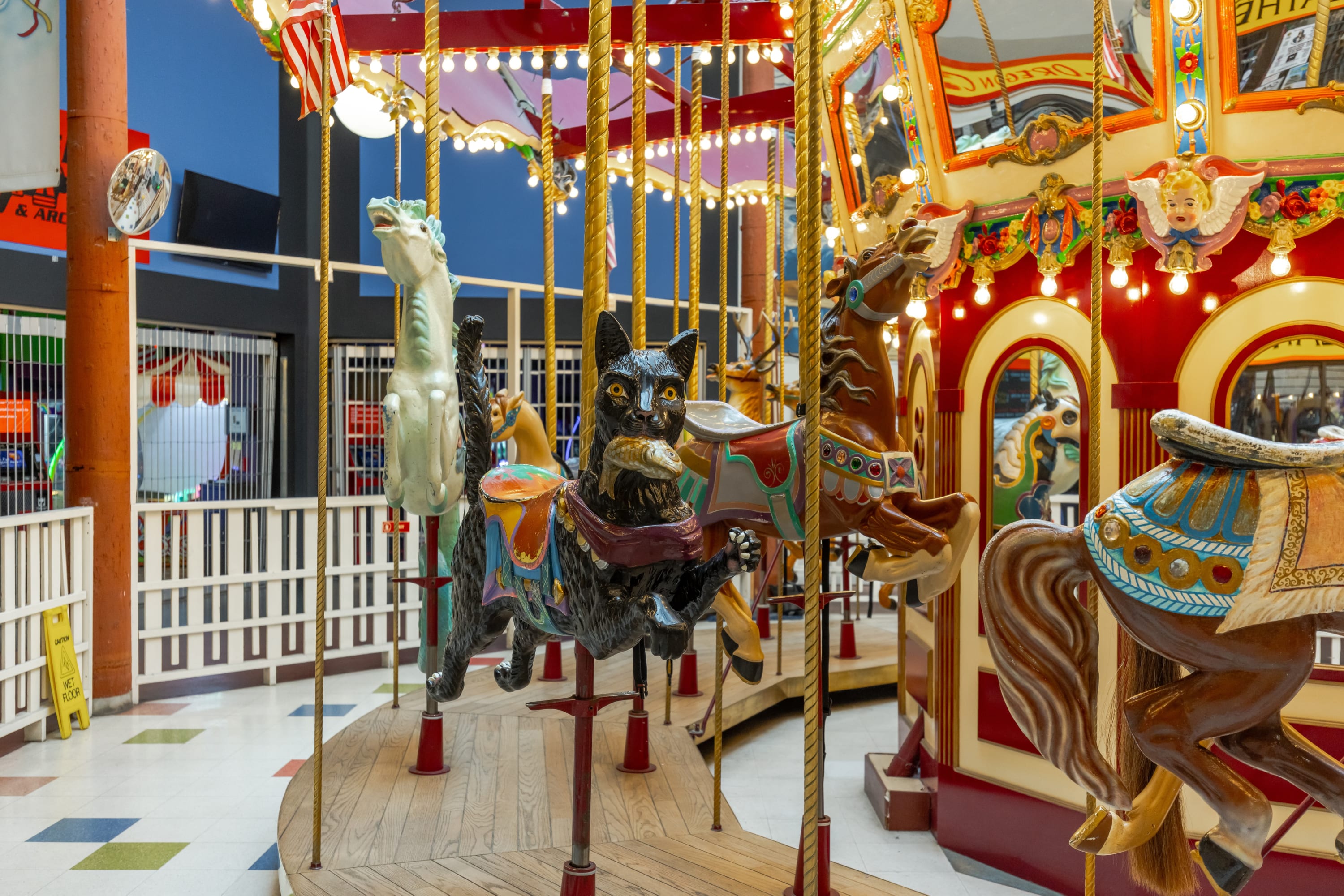 A close-up view of the carousel animals highlights a black cat and a brown horse, both intricately decorated with saddles and bridles. The vibrant colors and detailed craftsmanship are visible under the carousel's lights.