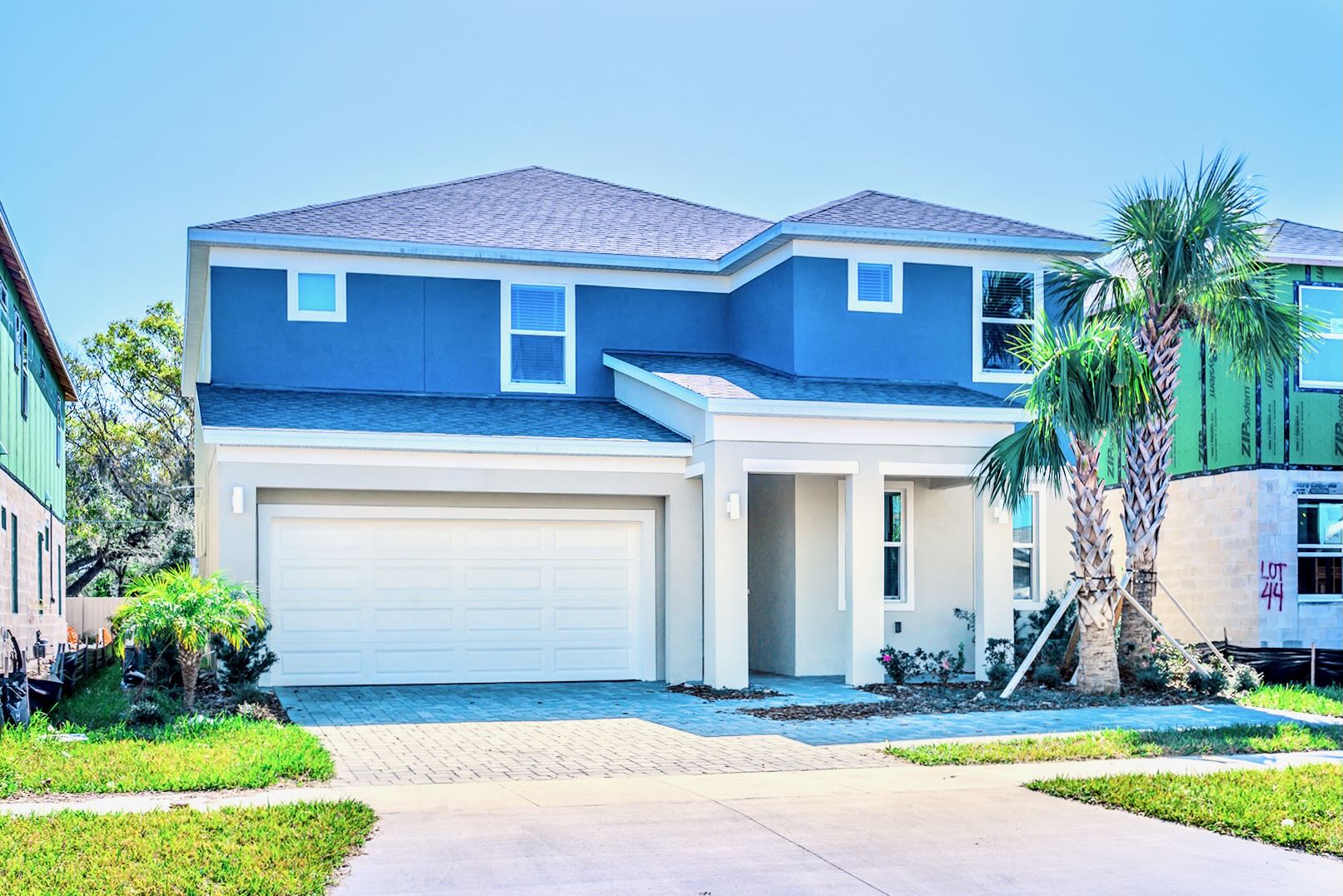 Stunning Modern Home With Sleek Blue Exterior, Spacious Driveway, And Tropical Palm Trees