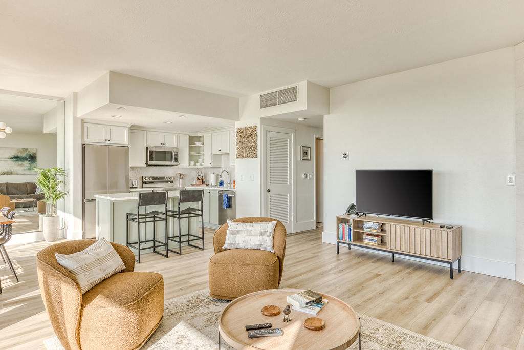 Open-concept living area with two mustard-colored armchairs and a round coffee table, transitioning into a modern kitchen with a light green island and white cabinetry, all on light hardwood floors.