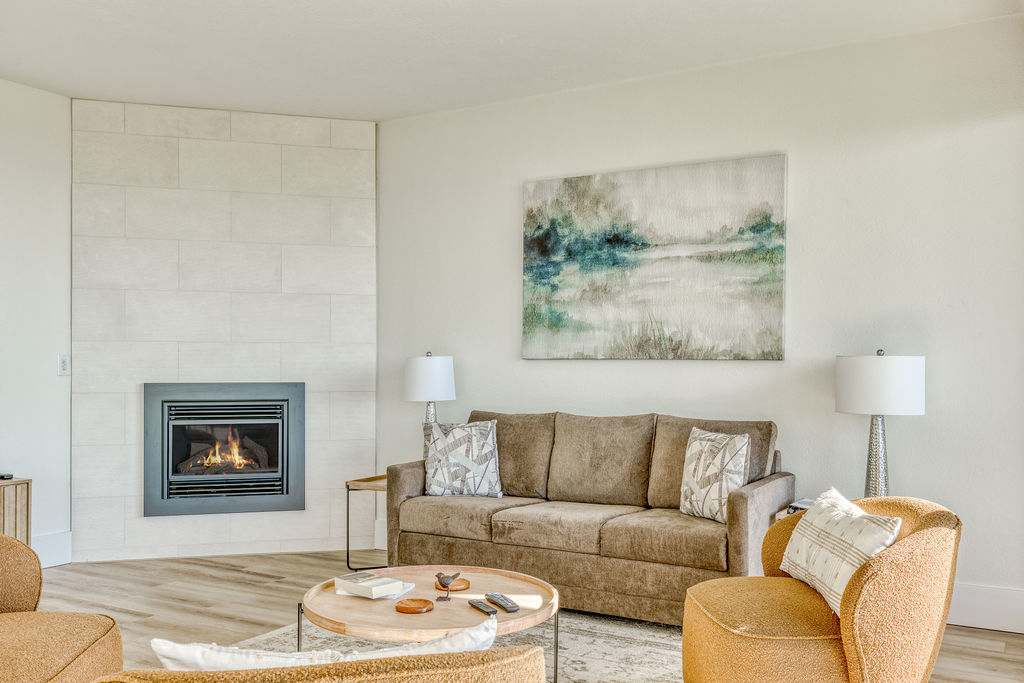 Close-up of a modern living room featuring a cozy fireplace with a light-tiled surround, a comfortable brown sofa with throw pillows, and an abstract landscape painting above.