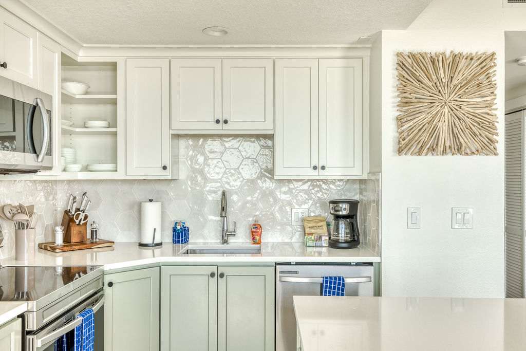Modern kitchen with light gray upper cabinets and sage green lower cabinets, white quartz countertops, a hexagonal white tile backsplash, and stainless steel appliances including a microwave, sink, and dishwasher.