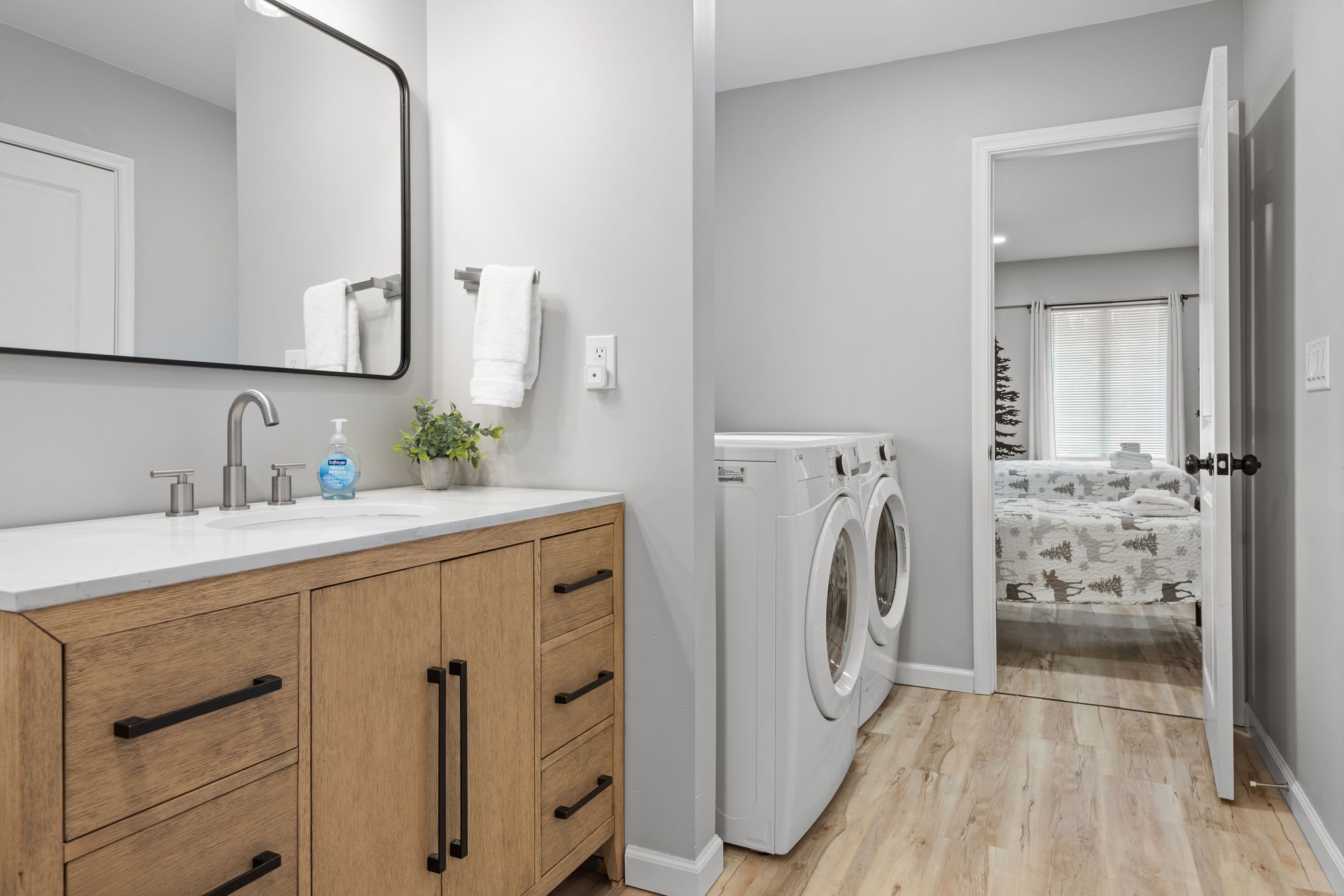 A sleek and stylish bathroom featuring a double vanity, natural wood cabinetry, and a fresh, open layout that connects conveniently to the laundry area.