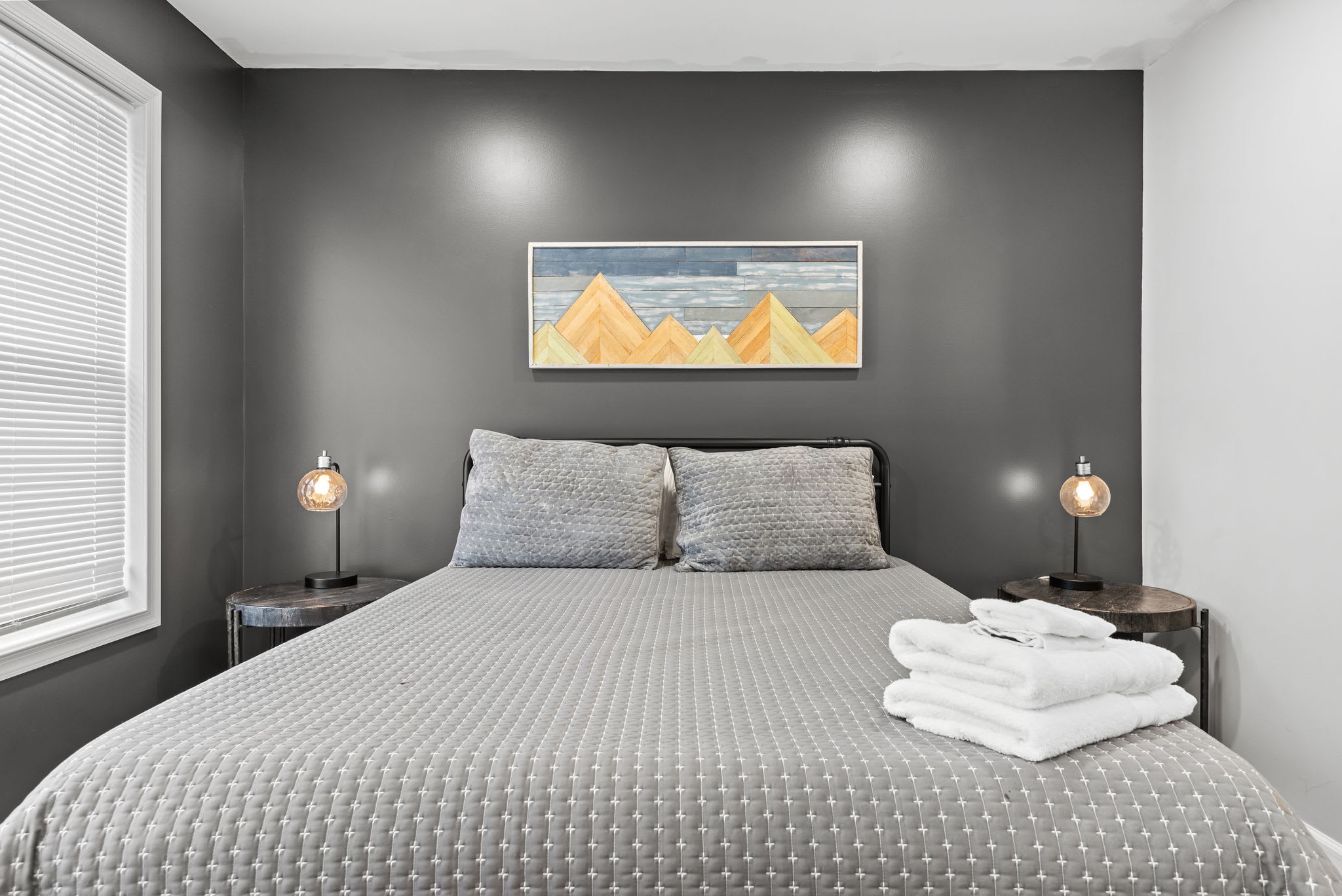 A stylish and serene bedroom featuring a dark accent wall, soft gray bedding, and warm lighting creating the perfect balance of modern elegance and comfort.