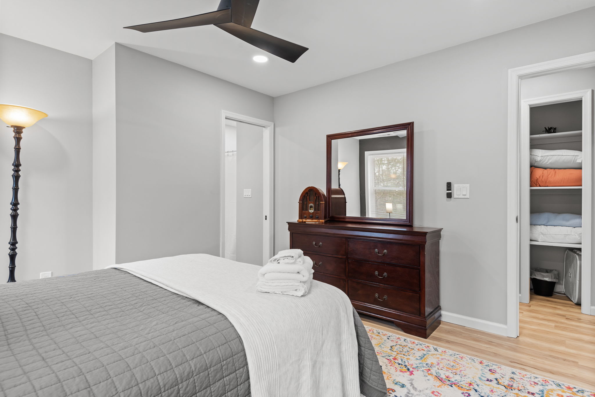 A bright and airy bedroom featuring a classic wooden dresser, modern ceiling fan, and cozy neutral tones, creating a restful and inviting atmosphere.