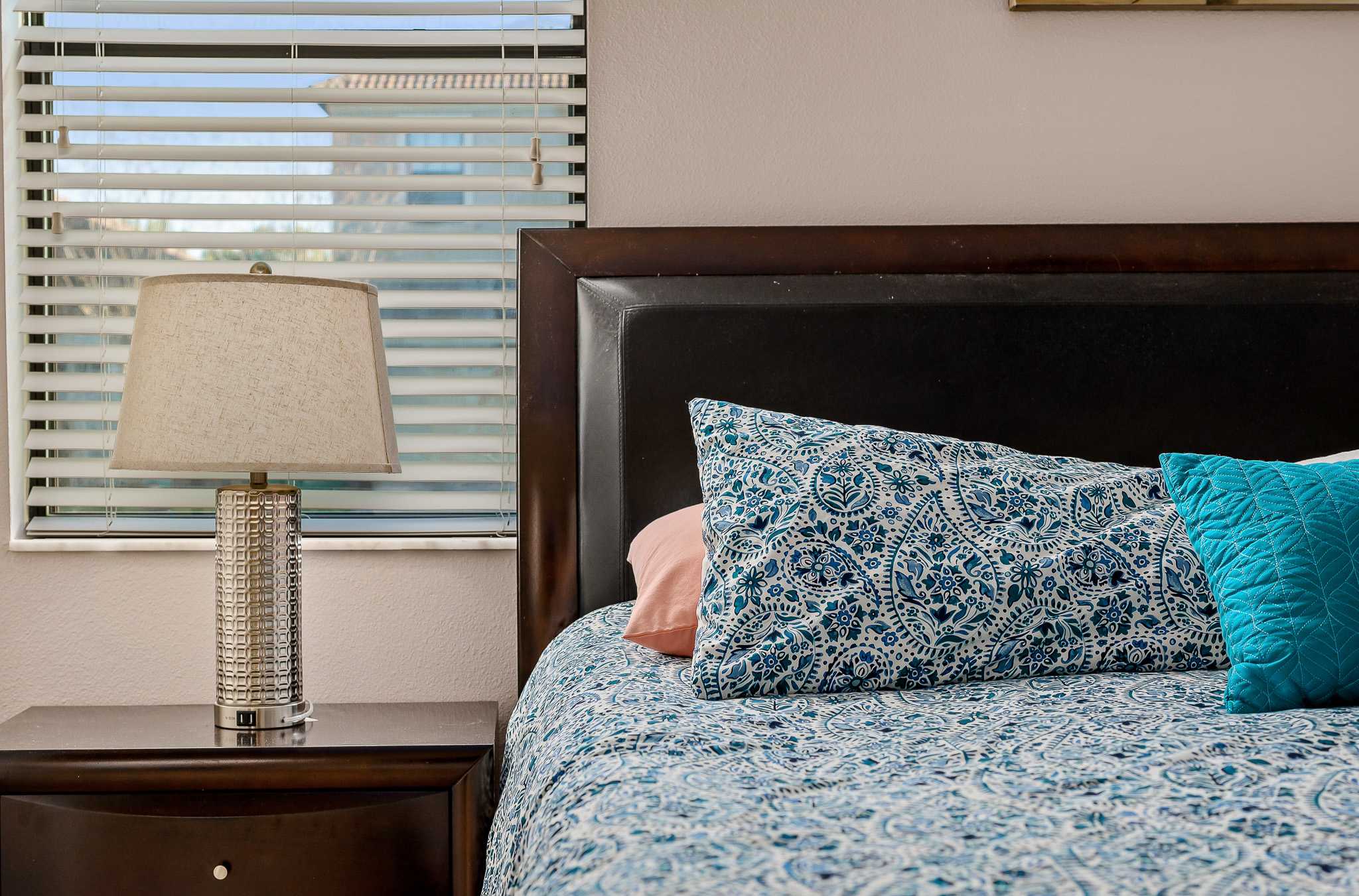 Bedside view w/ lamp and soft textures, calm and comfortable.