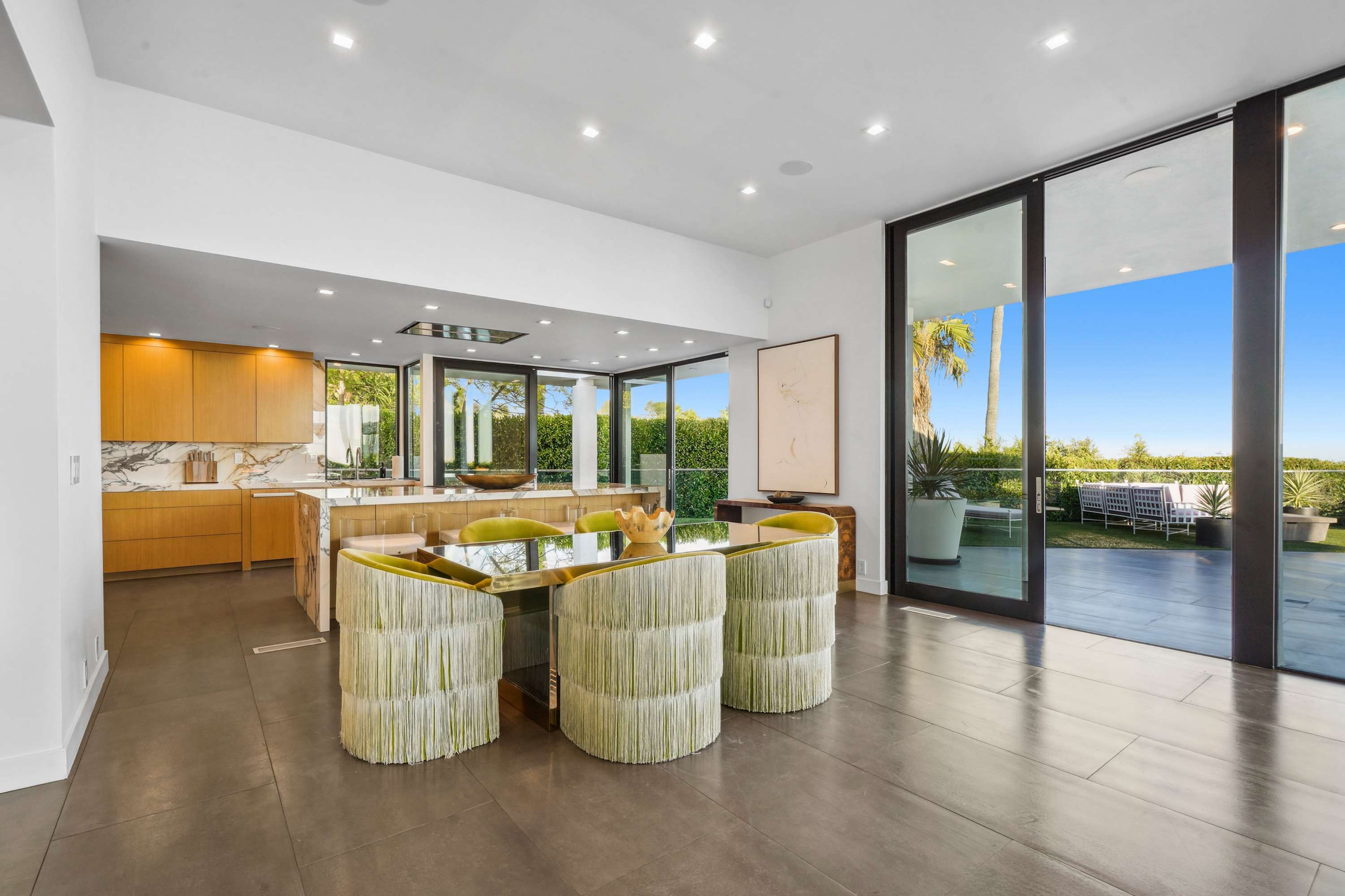 Bold, fringed seating around a custom glass table, bathed in natural light and elegance.