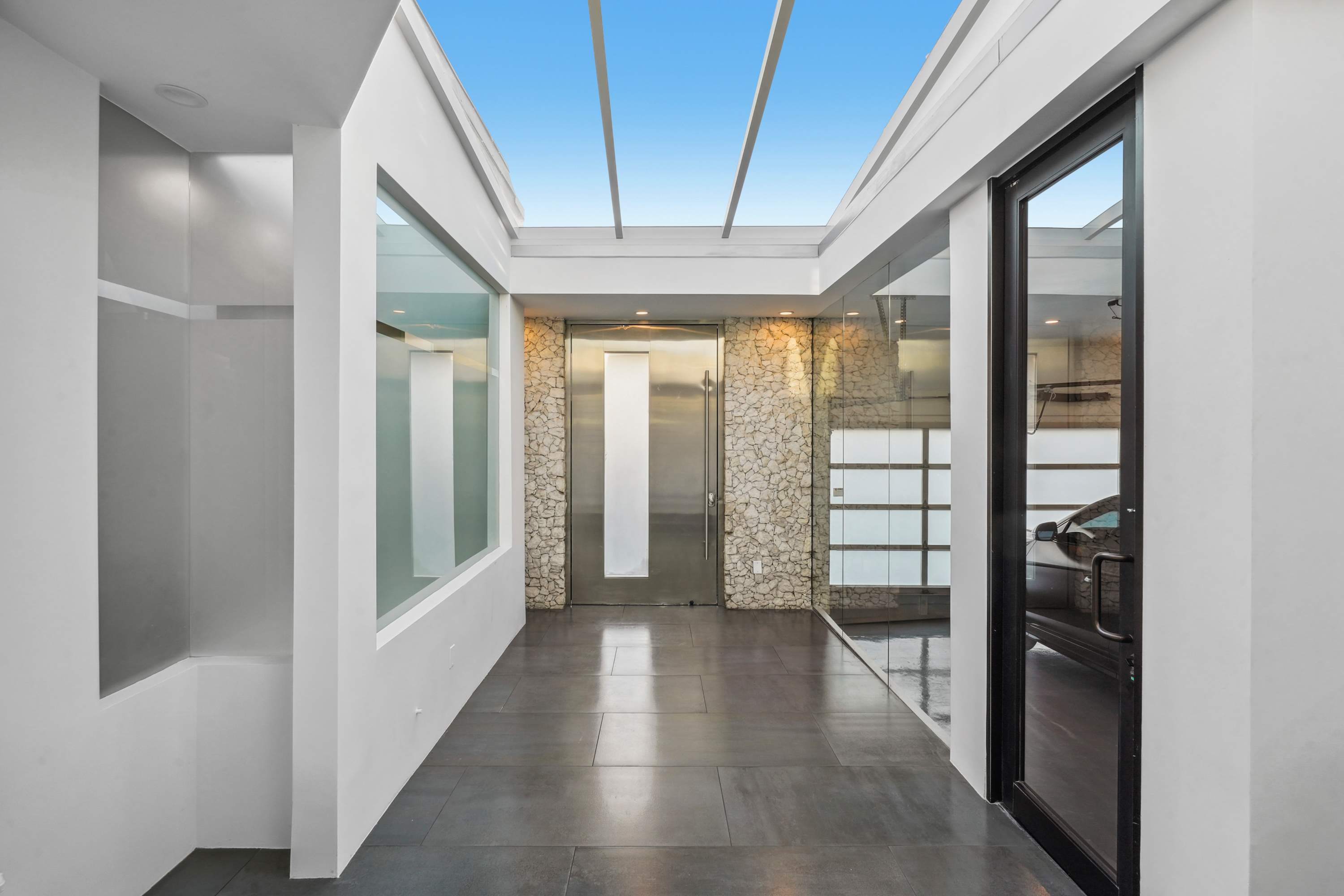 Step into a grand, sky-lit entry framed by sleek glass and stone, where luxury and style converge.