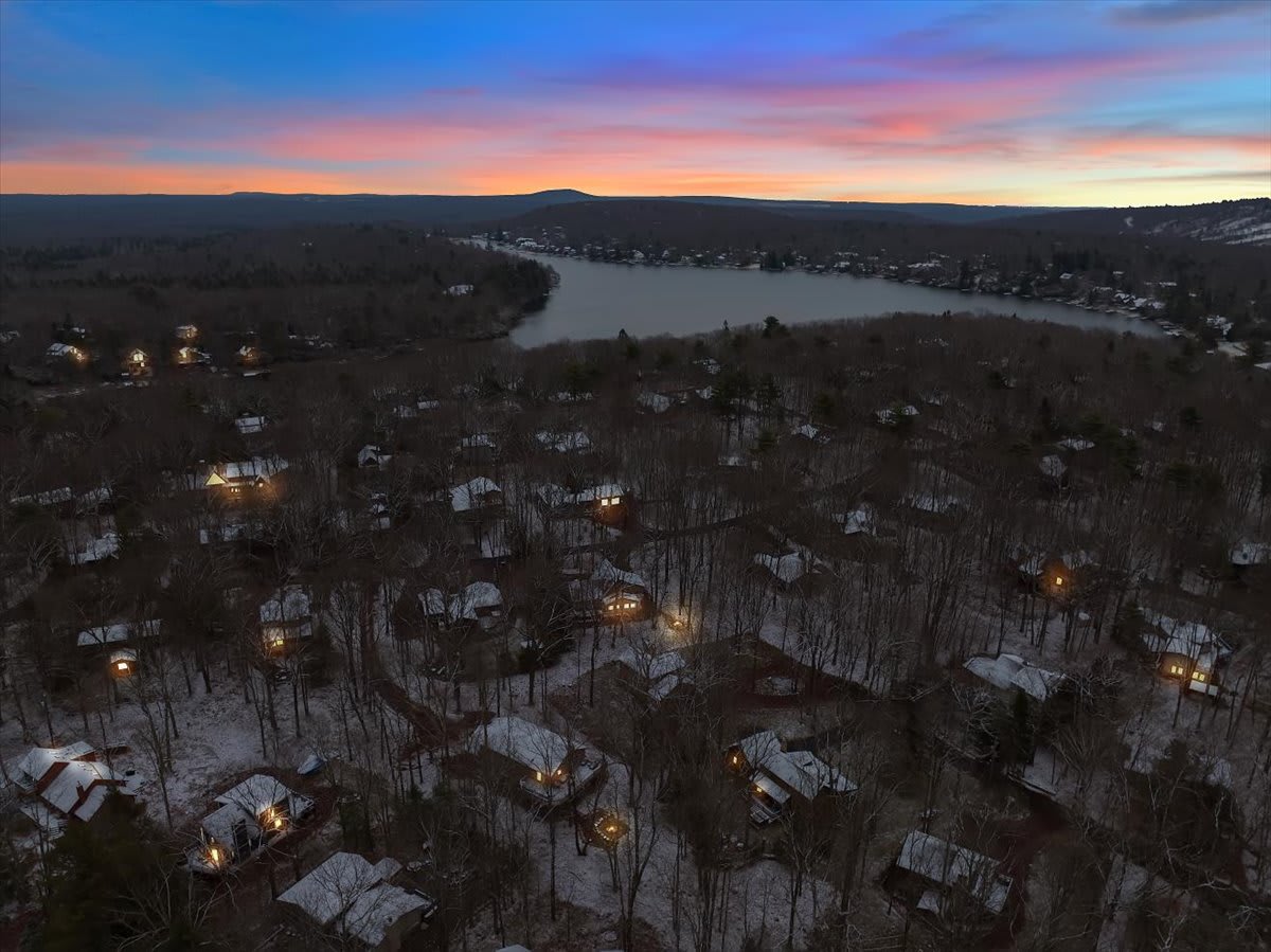Enchanting Aerial Twilight View – A breathtaking bird’s-eye view of the lakeside community at sunset, with glowing homes nestled among the trees and the water reflecting the last light of the day.