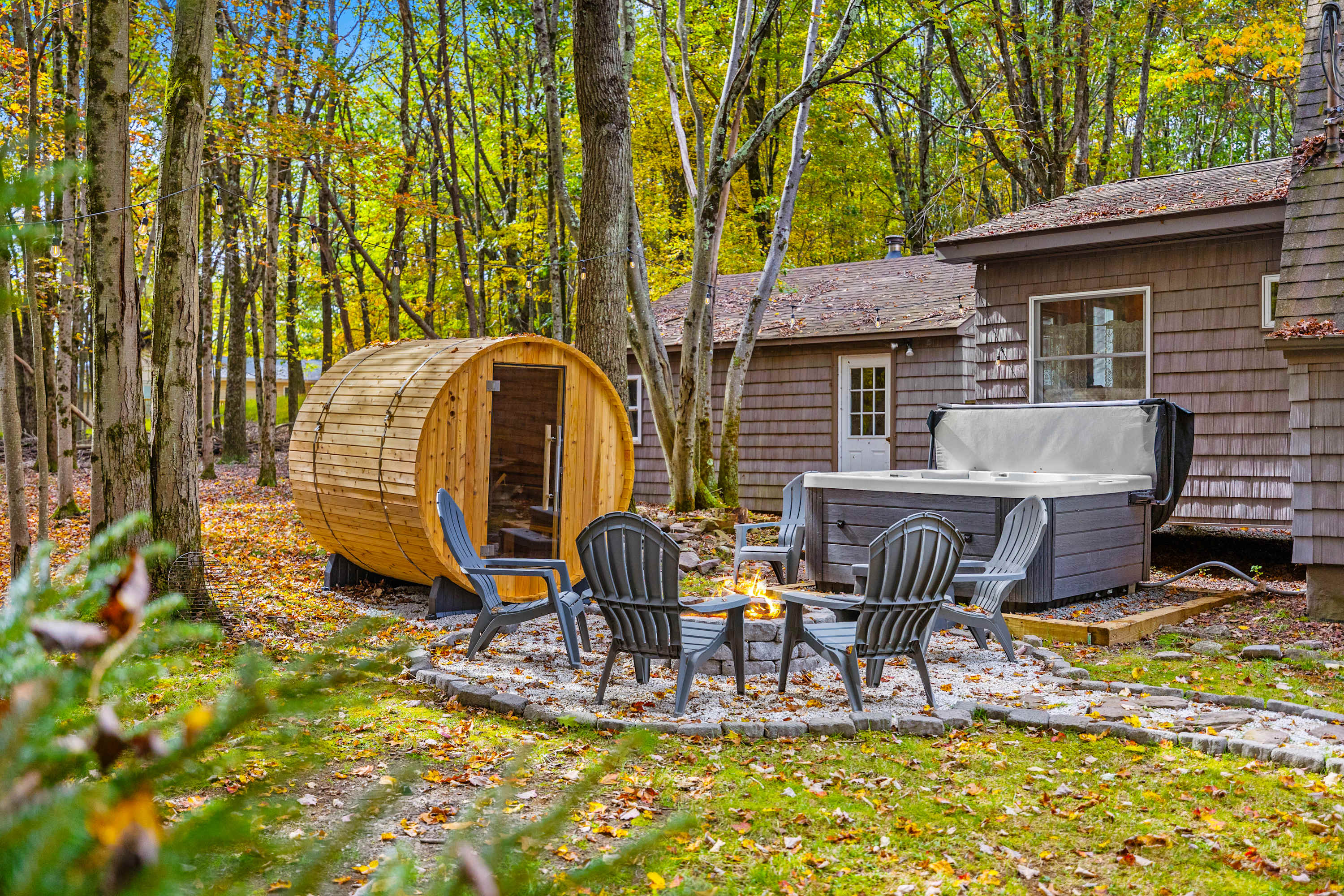 Enjoy ultimate relaxation in this backyard sanctuary featuring a barrel sauna, bubbling hot tub, and cozy fire pit. Adirondack chairs offer a comfortable spot to soak in the surrounding nature.