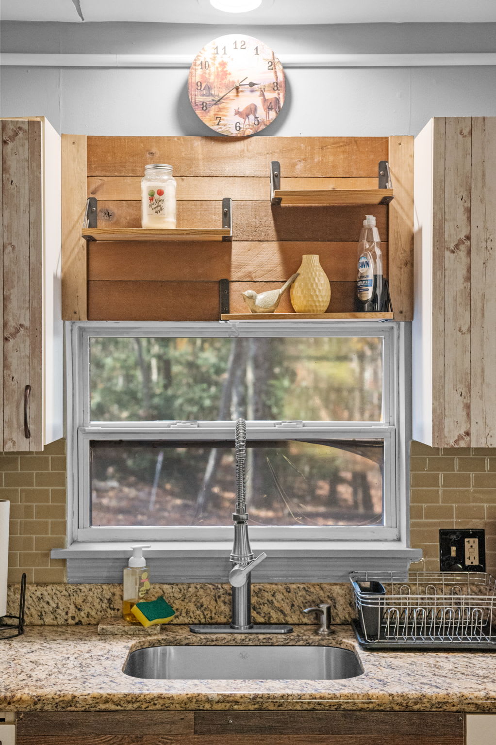 Above the sink, open shelving and a charming clock frame the wooded view, adding a personal touch to the overall design.