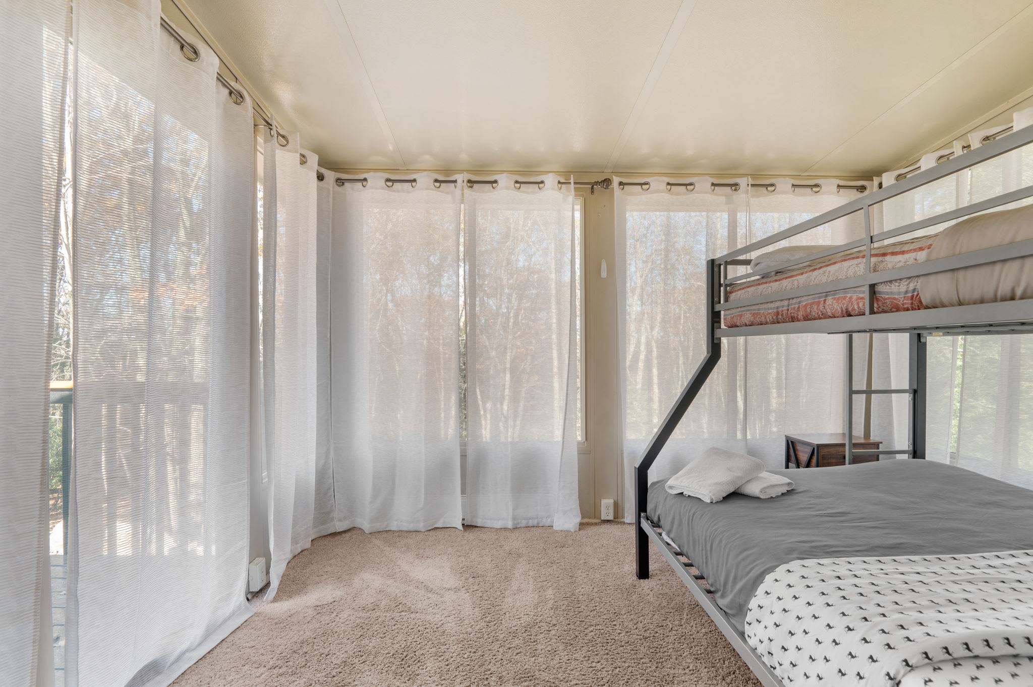 Floor-to-ceiling windows let natural light flood the space, highlighting soft carpeting underfoot.