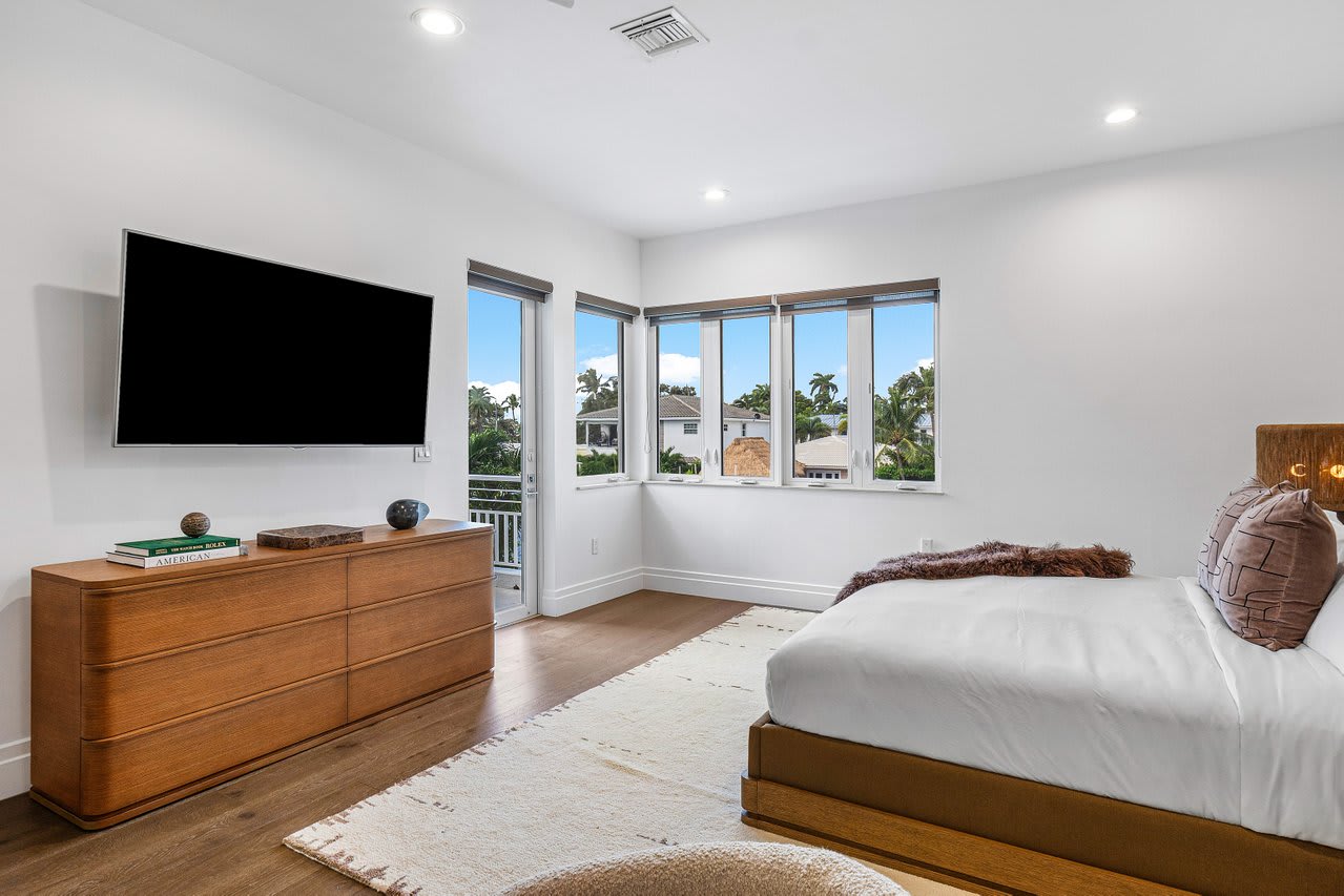 Bright and airy bedroom with sleek wooden furnishings, soft rugs, and serene views from large windows.