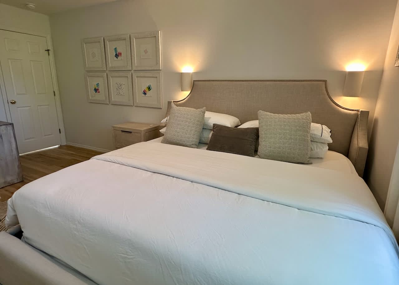 Bedroom with an upholstered headboard, pale blue linens, and sconce lighting.