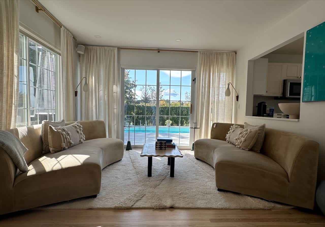 Living room seating area with tan curved sofas and a view of the pool through floor-to-ceiling windows.