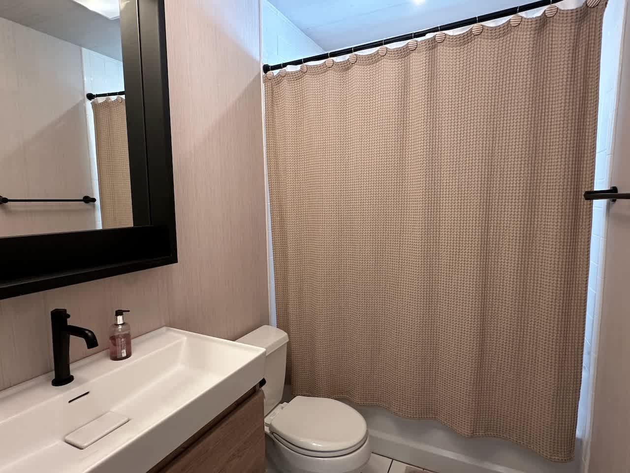 Bathroom with a floating vanity, wall-mounted mirror, and curtained shower-tub combo.