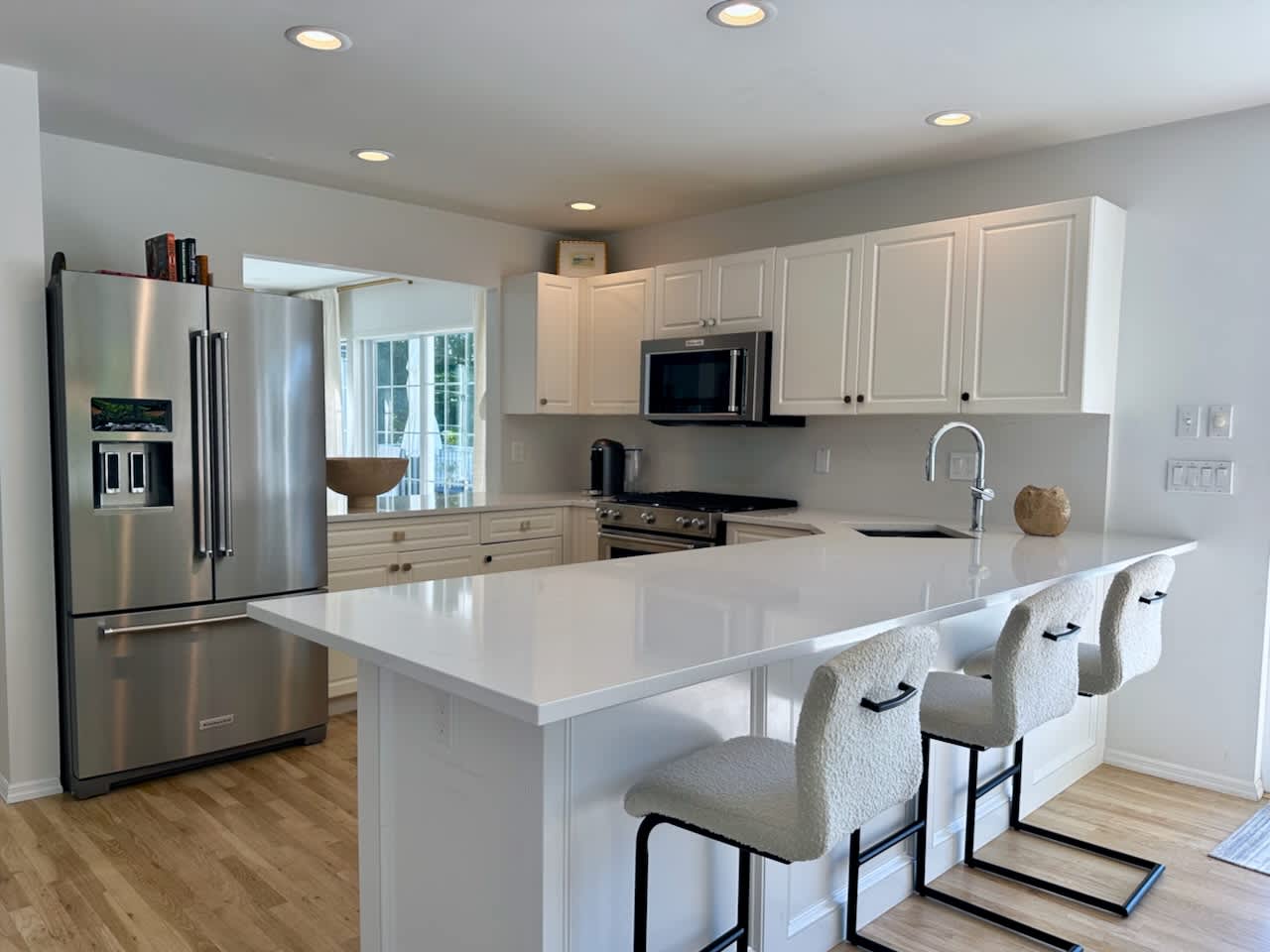 Kitchen with a white quartz island, upholstered counter stools, and a stainless refrigerator.