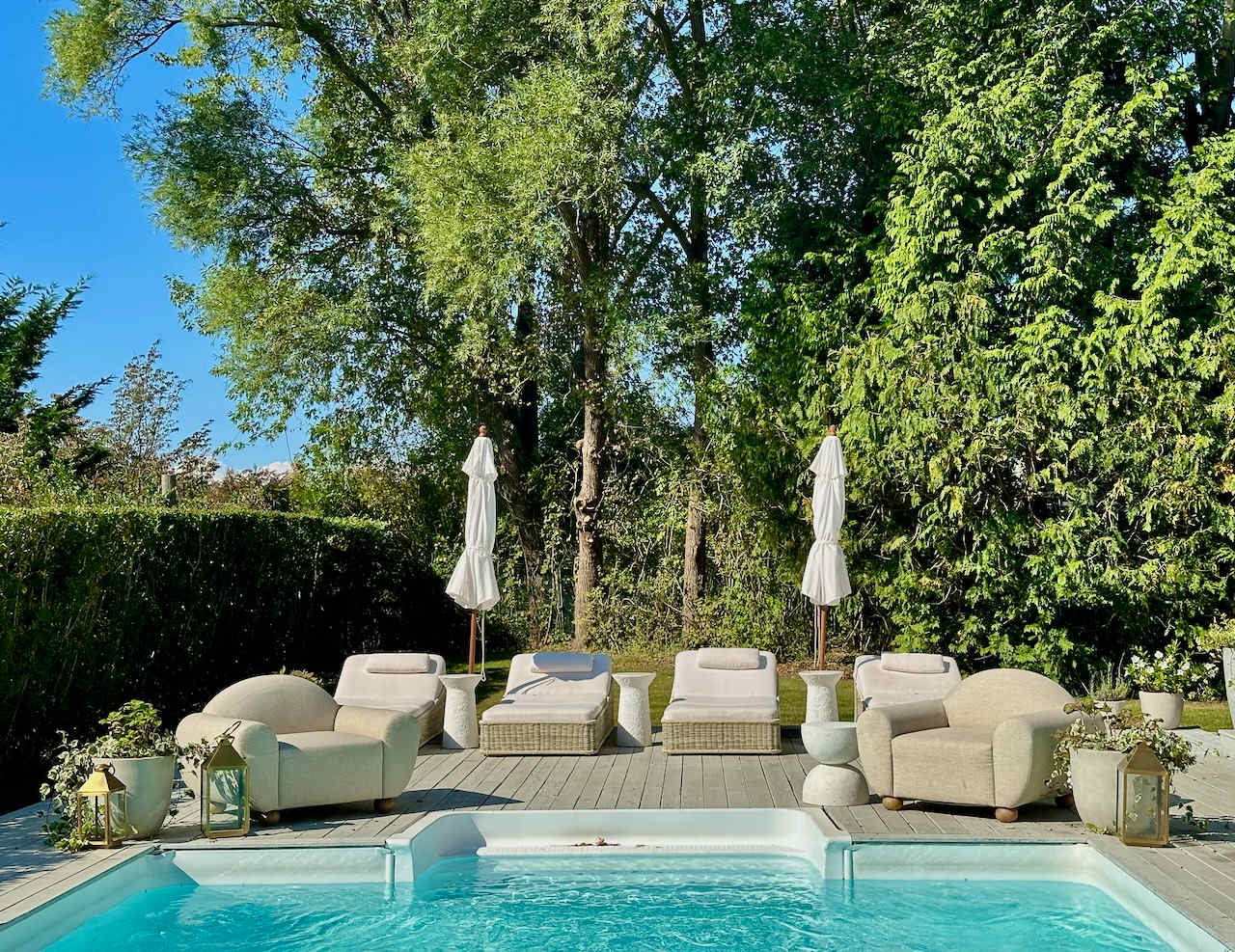Pool deck lounge chairs and umbrellas shaded by trees along the property's edge.