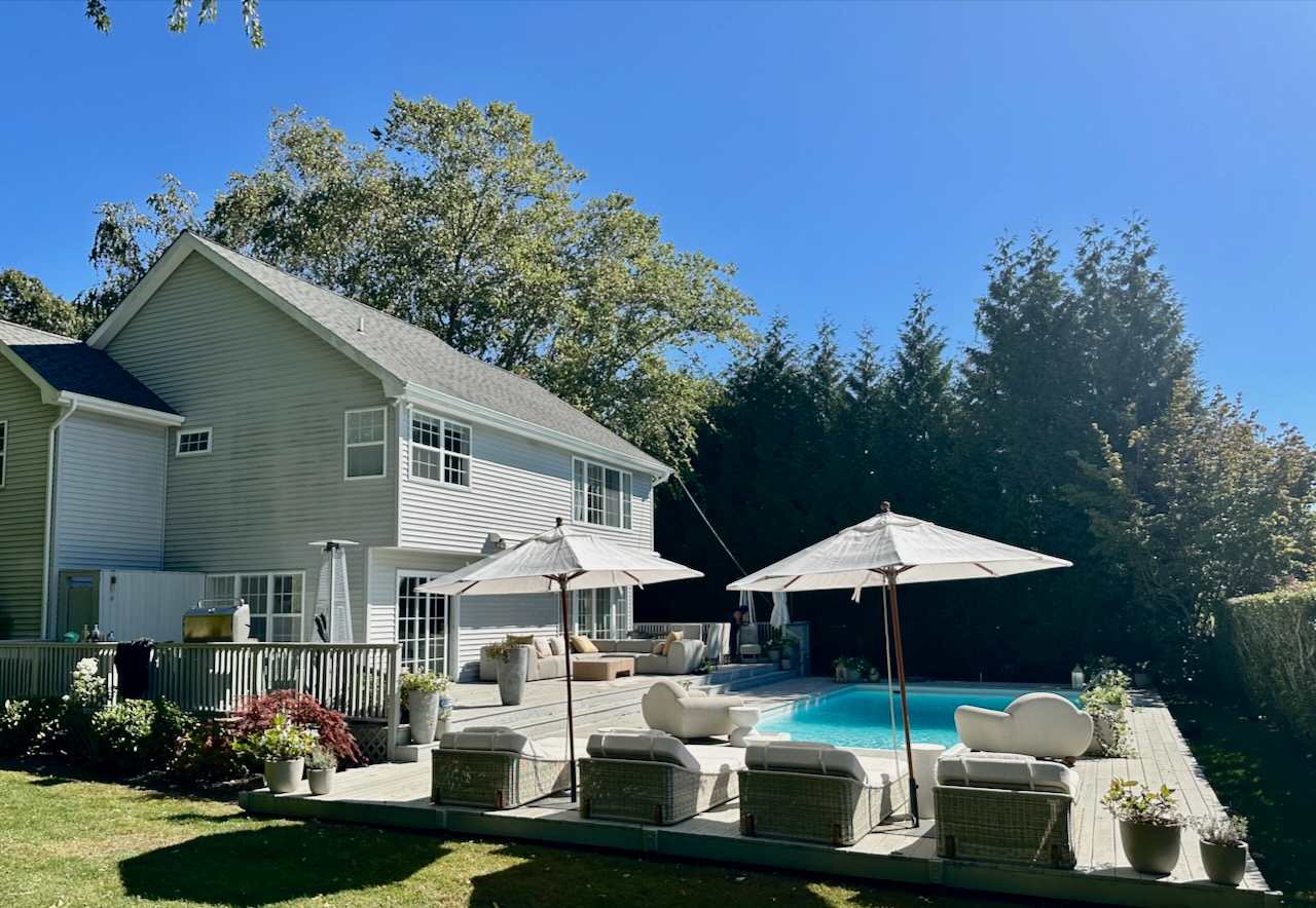 View of the house exterior from the pool deck with lounge seating and umbrellas.