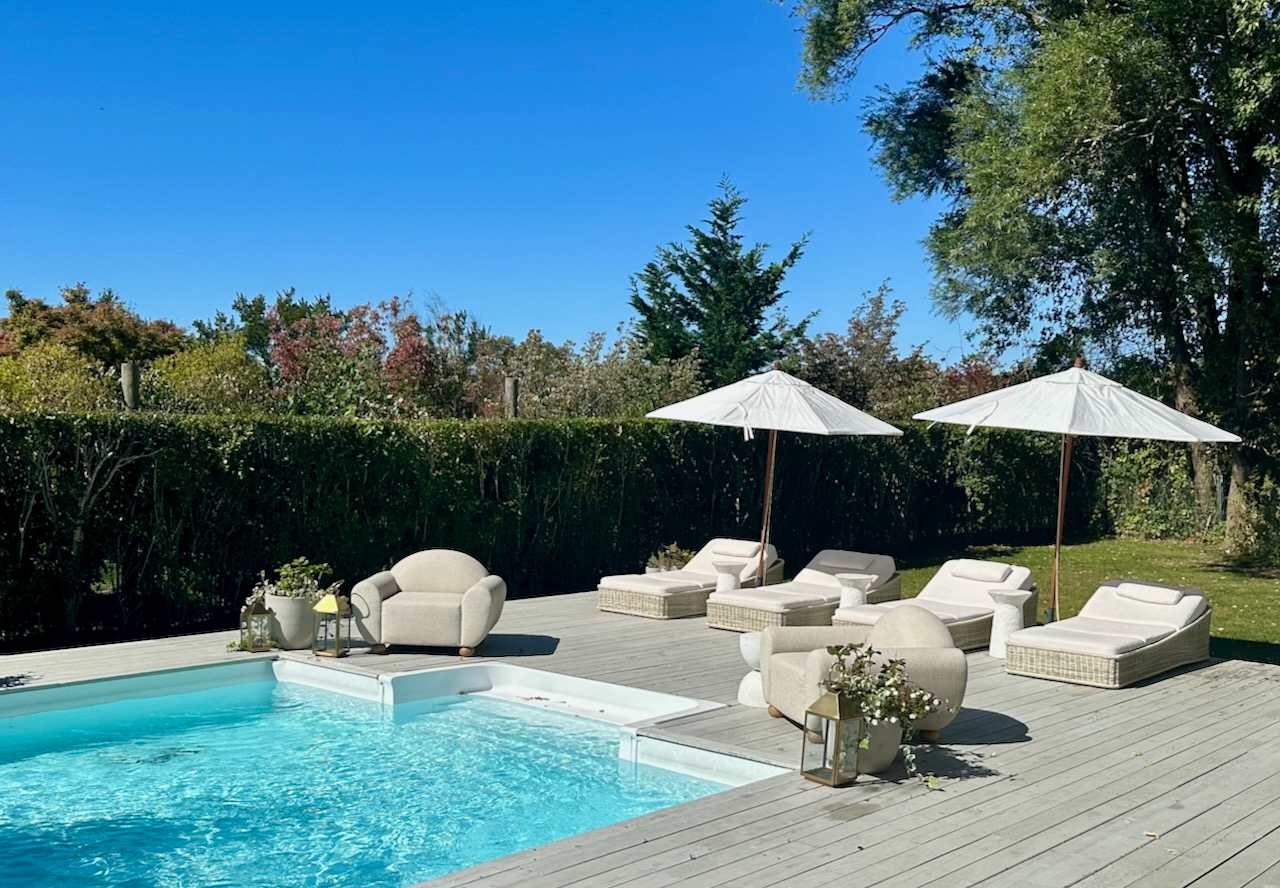 Pool deck seating with umbrellas and lounge chairs framed by tall hedges.