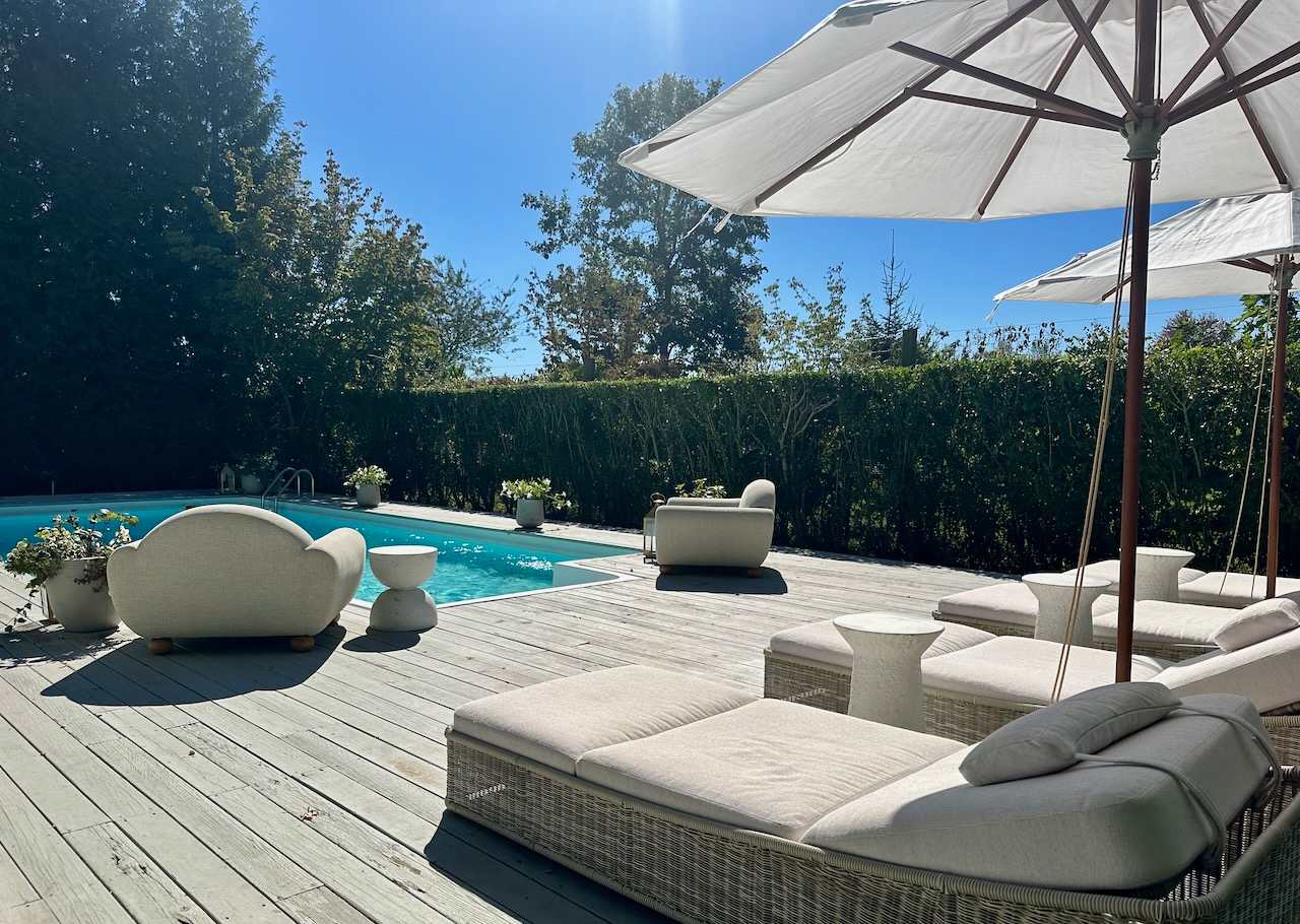 Poolside daybeds and lounge chairs under umbrellas beside the hedge-lined pool.