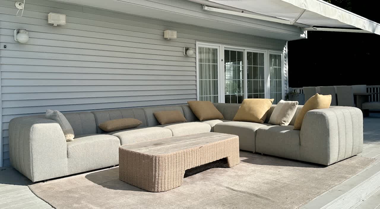 Covered patio sectional sofa with a wicker coffee table against the house's siding.