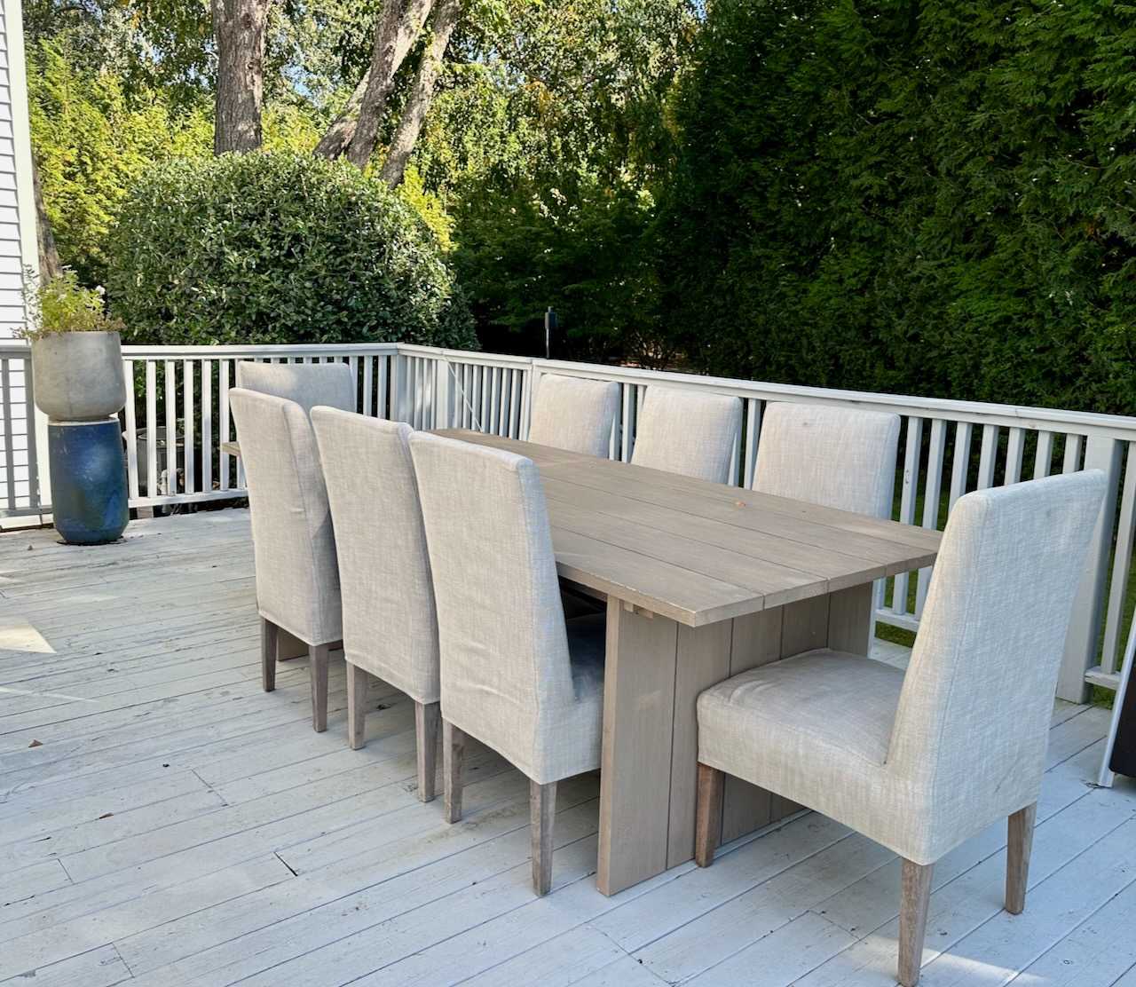 Outdoor dining table with upholstered chairs set on the deck overlooking the yard.