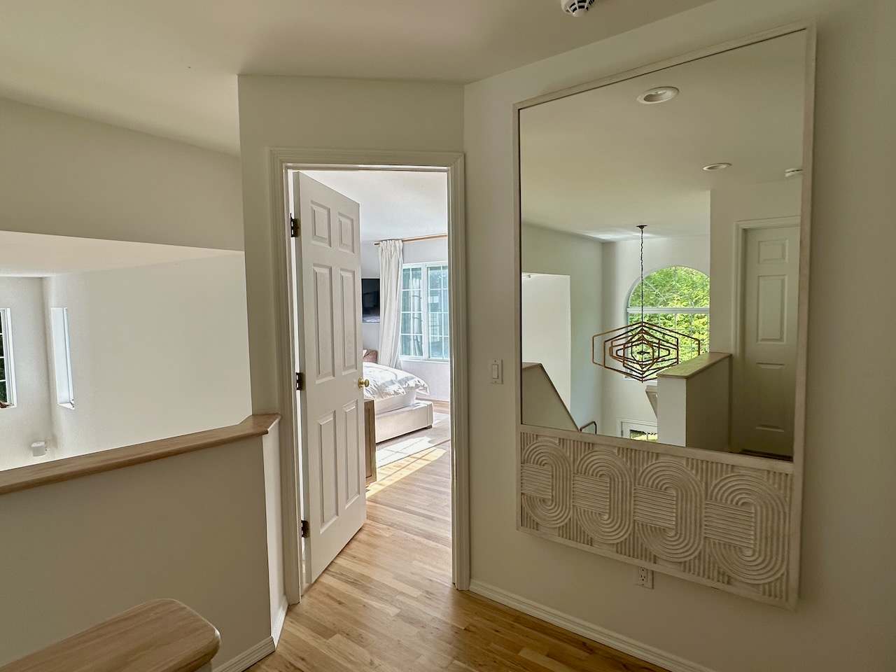 Upstairs hallway landing with a mirror and a view into an adjoining bedroom.
