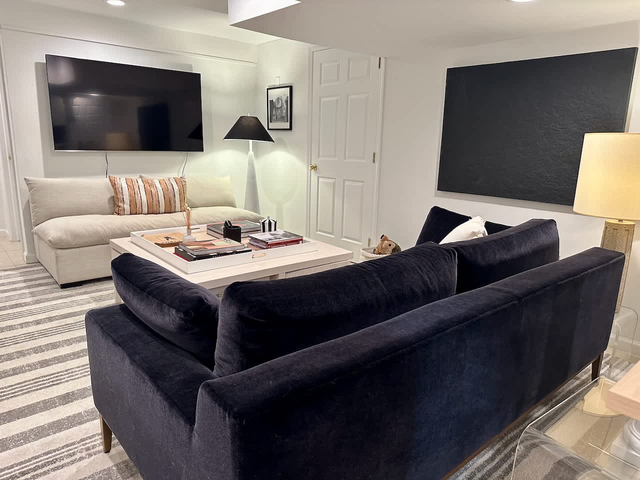 Media room with a navy sofa, wall-mounted TV, and layered artwork on the wall.