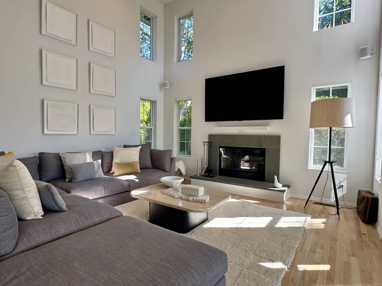 Double-height living room with a gray sectional sofa, fireplace, wall-mounted TV, and gallery wall.