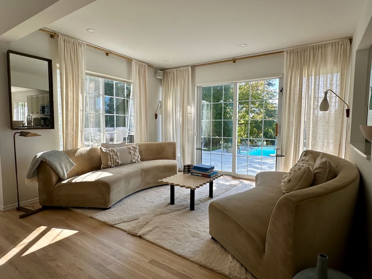 Living room with curved tan sofas and sliding glass doors overlooking the pool.