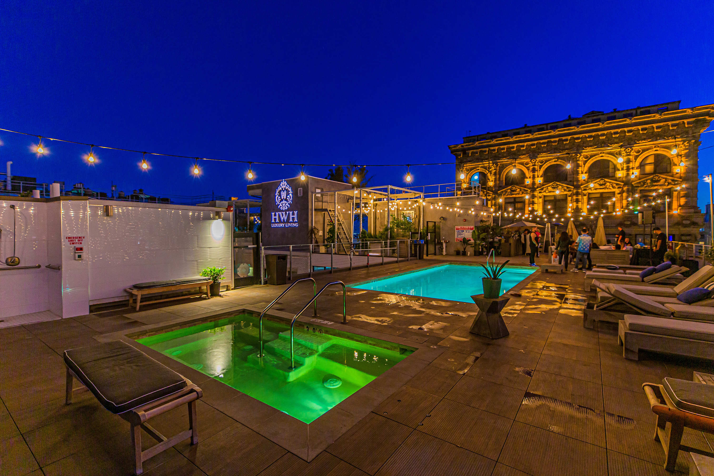 A nighttime view of a rooftop pool with lounge chairs and string lights