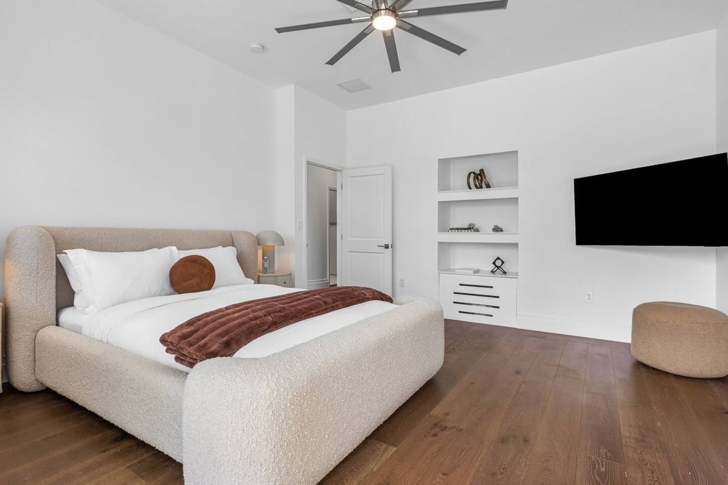 Sink into comfort in the stylish guest bedroom, featuring soft textures, warm wood floors, and built-in shelving.