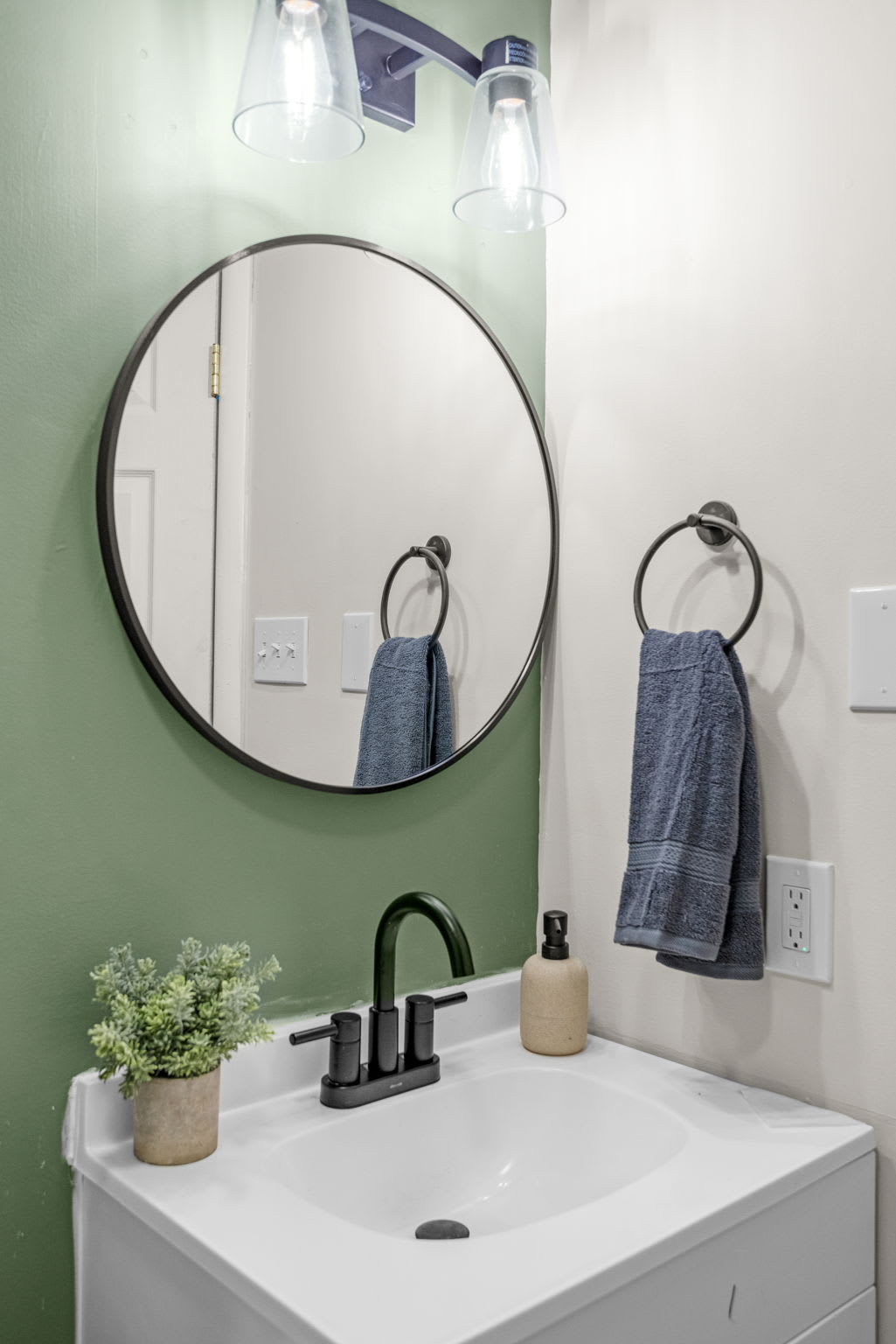 Chic & Refreshing Bathroom Space – A bright and airy bathroom with a round mirror, stylish green walls, and modern black fixtures, creating a spa-like atmosphere.