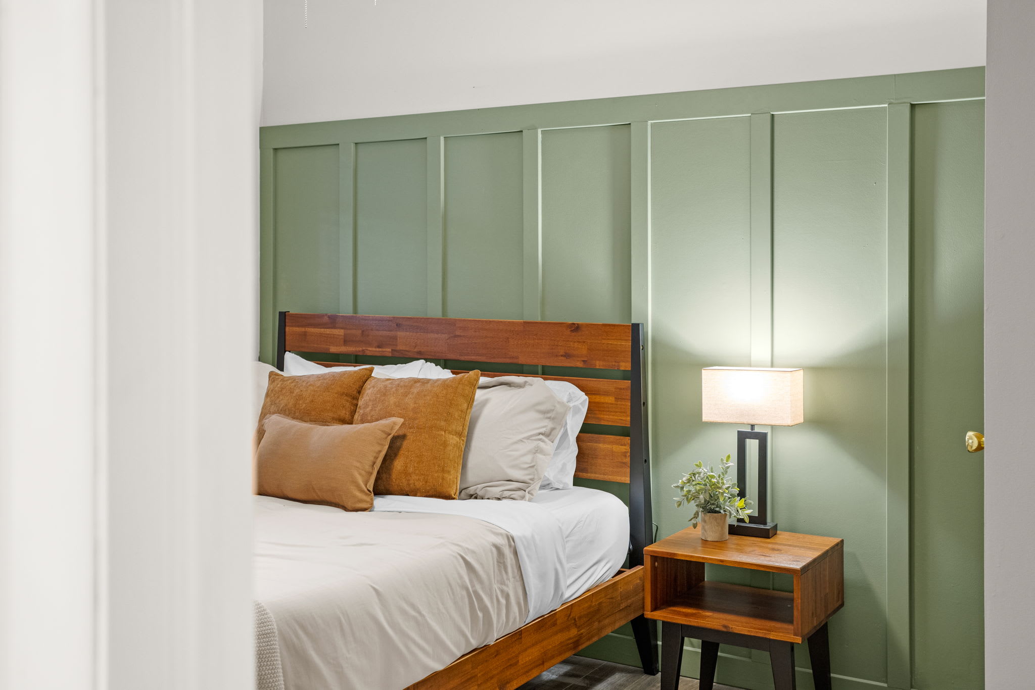 A beautifully designed bedroom with earthy green paneling, soft lighting, and complementary warm-toned pillows.