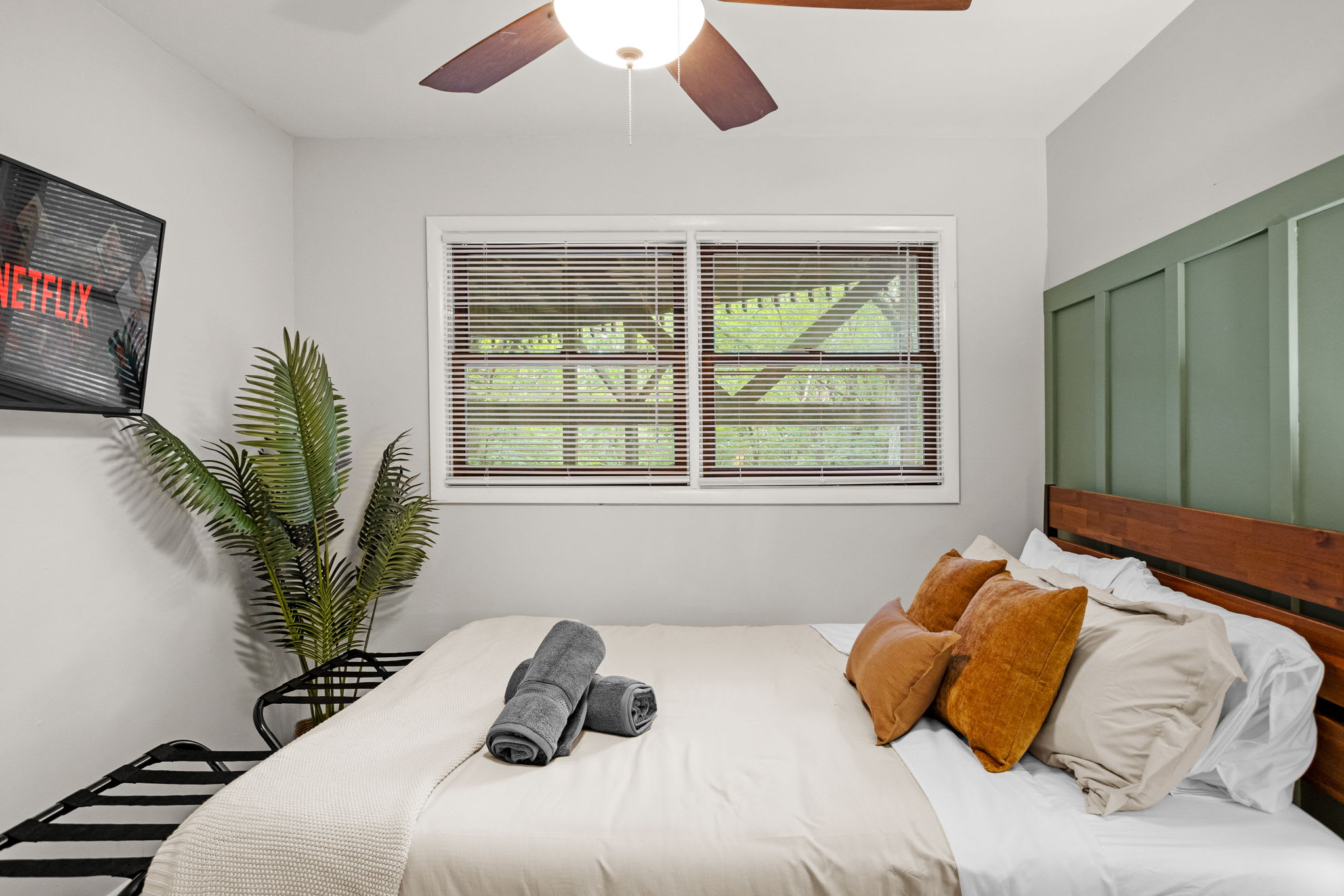 A chic bedroom featuring a mounted TV, lush greenery, and a stylish neutral bedding arrangement.