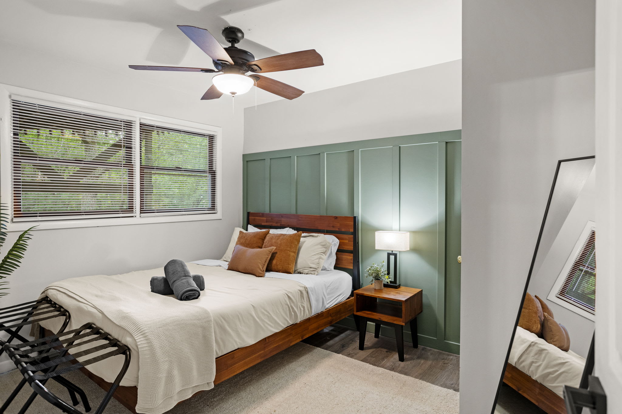 A modern bedroom with large windows, a ceiling fan, and a cozy bed setup, perfect for relaxation.