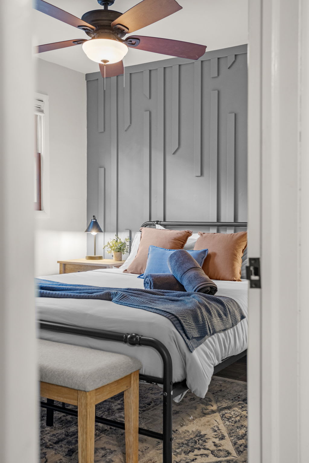 A tastefully designed bedroom featuring cool-toned paneling, plush pillows, and modern bedside decor.