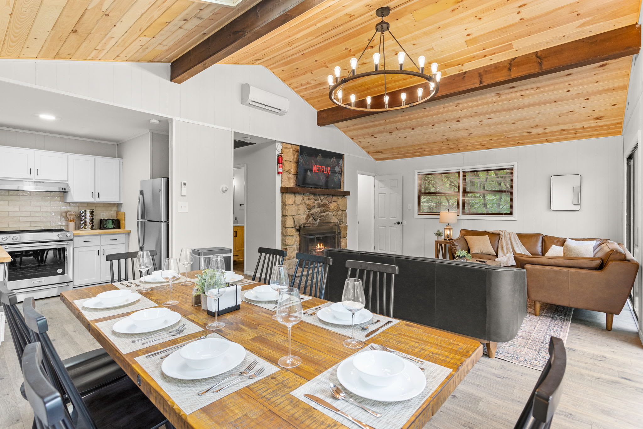 A spacious dining and living room featuring a high wooden ceiling with a chandelier, seamlessly blending rustic and modern styles.
