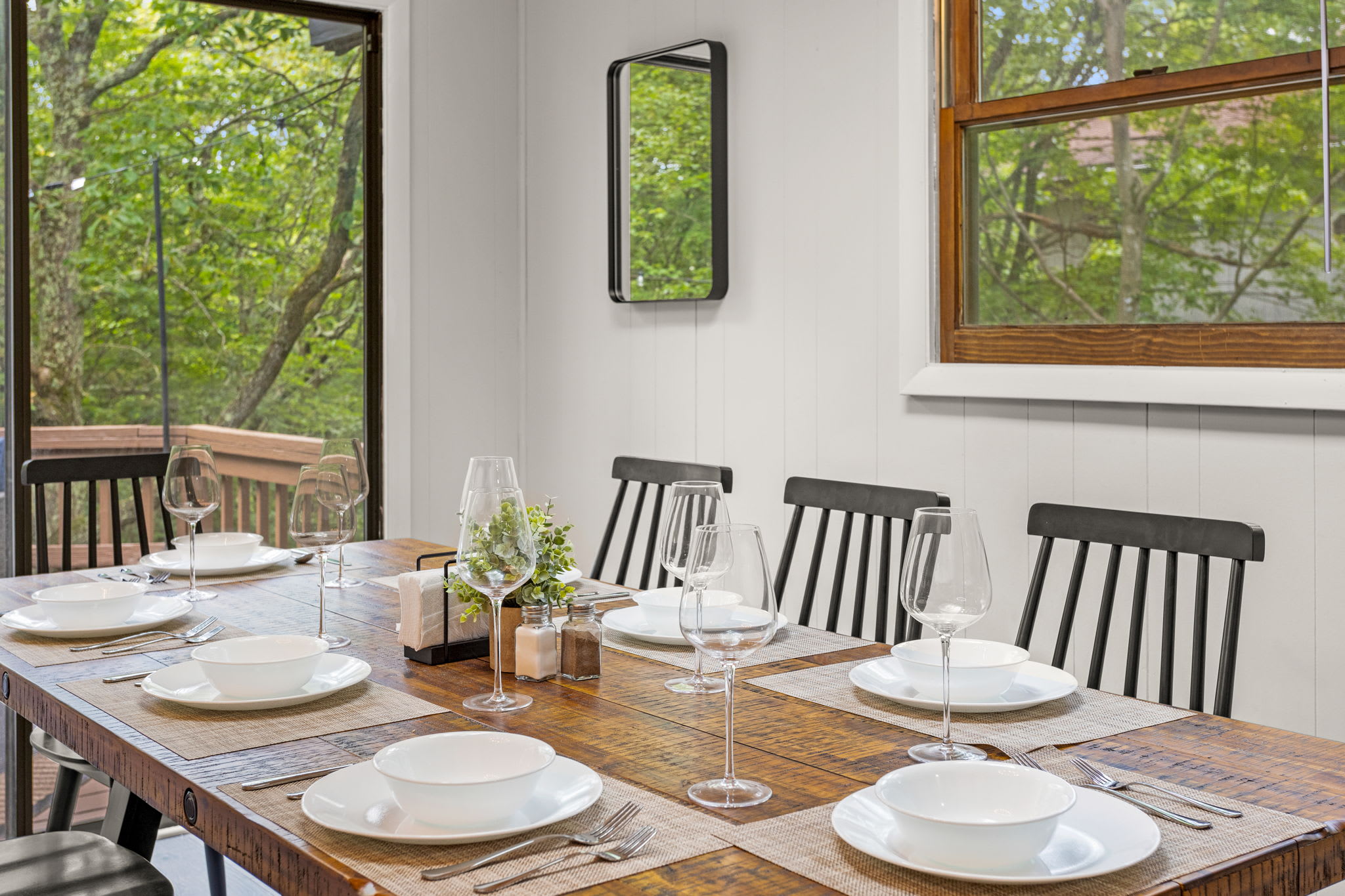 Elegant Dining Setup – A wooden dining table set for a meal, surrounded by sleek black chairs and a window with scenic outdoor views.