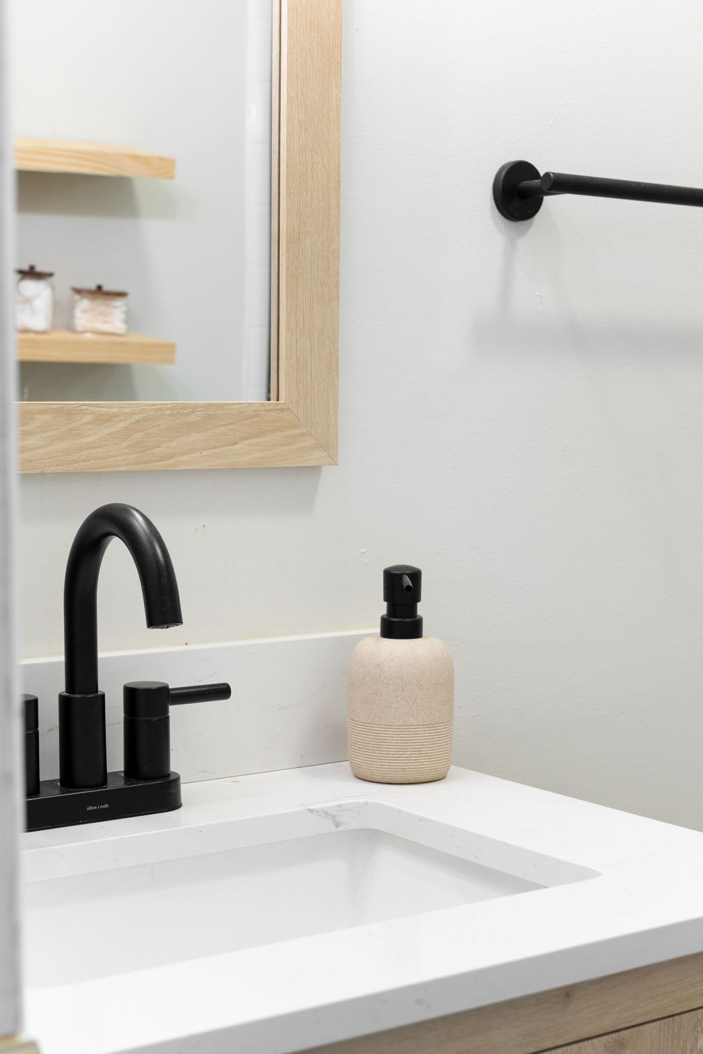 A sleek bathroom vanity with a black faucet, minimal decor, and a stylish wood-framed mirror.