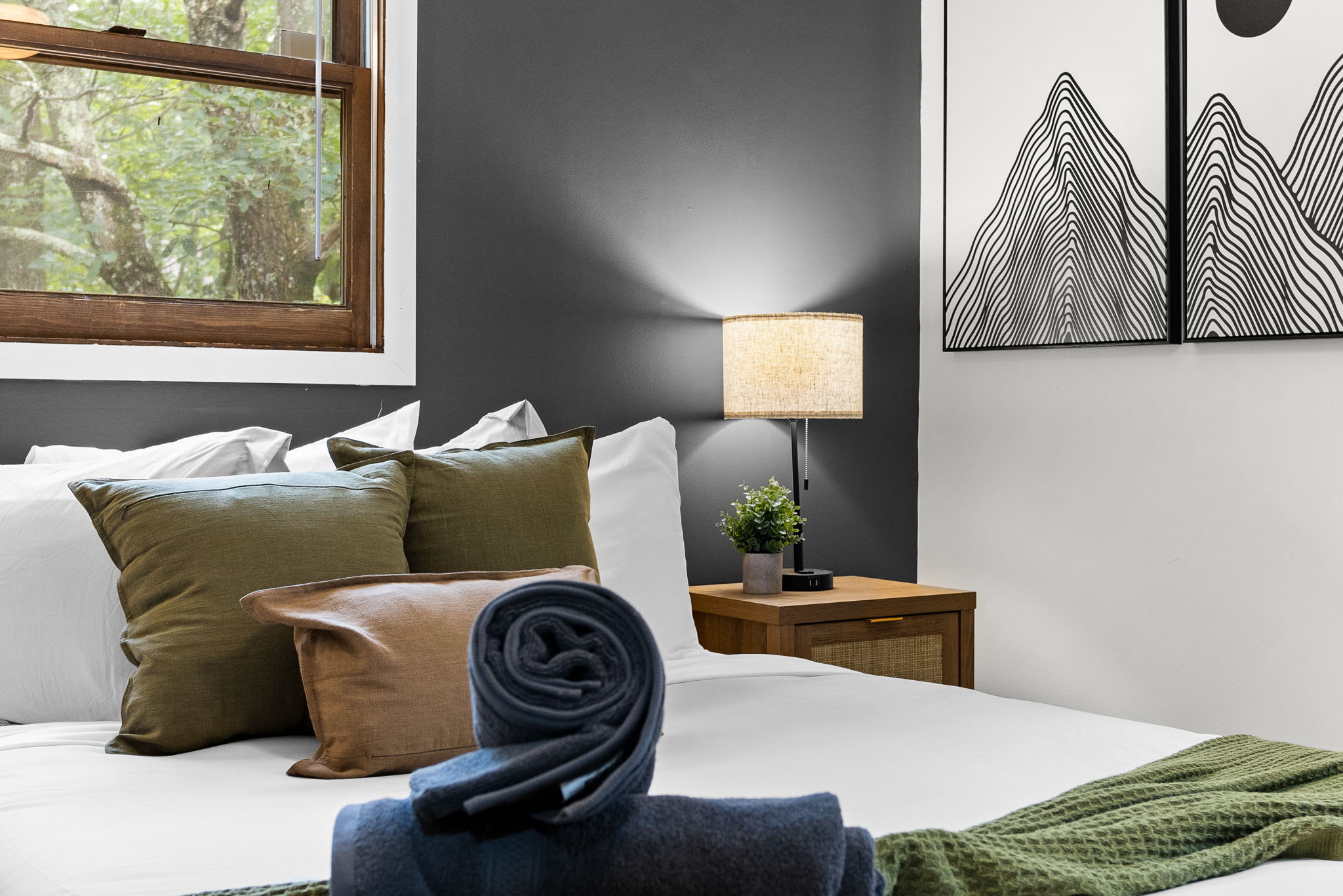 A chic room with a gray accent wall, decorative pillows in green and mustard tones, and a cozy nightstand setup.