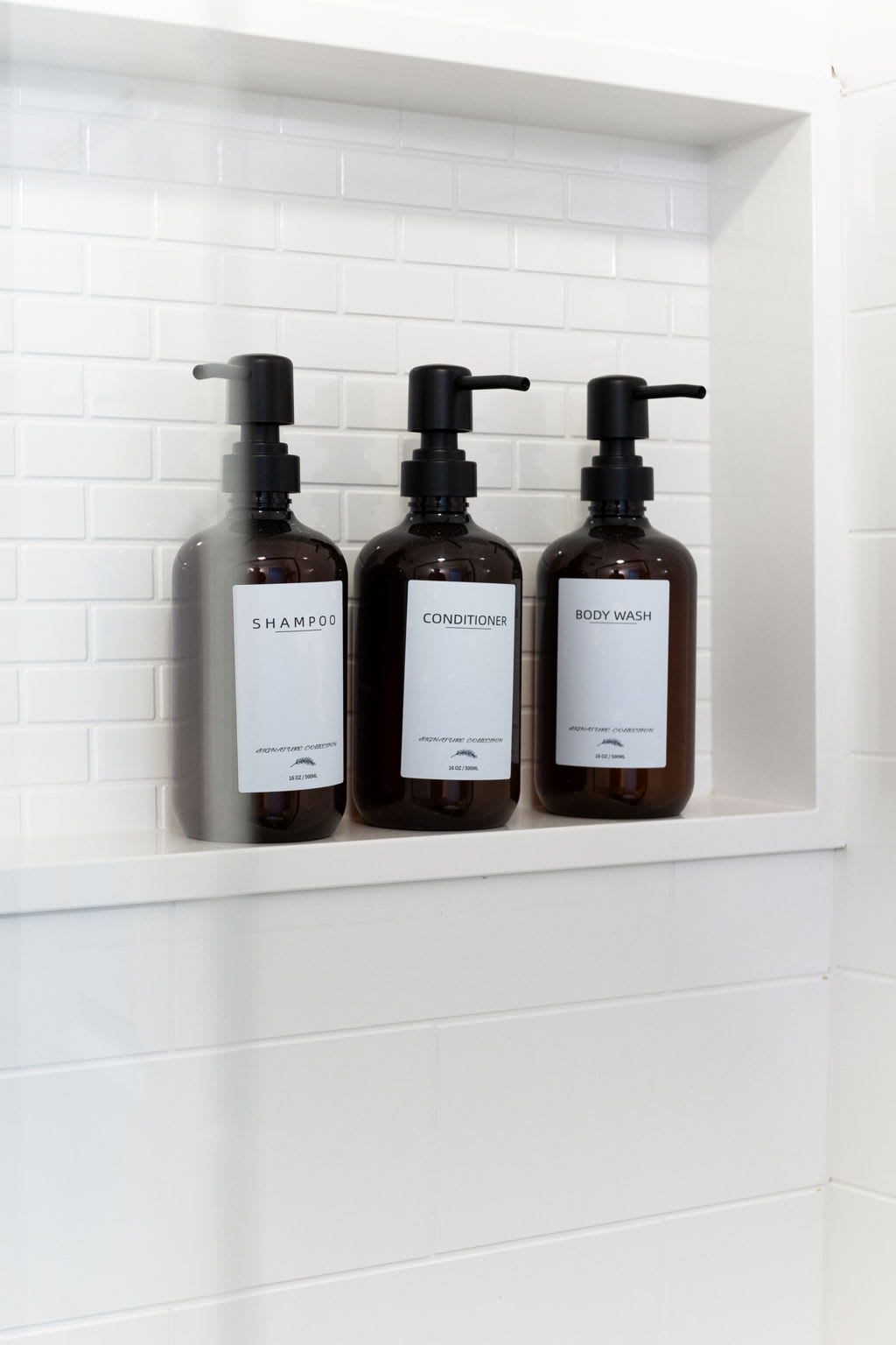A close-up of a clean and minimal shower shelf with neatly arranged black soap dispensers.